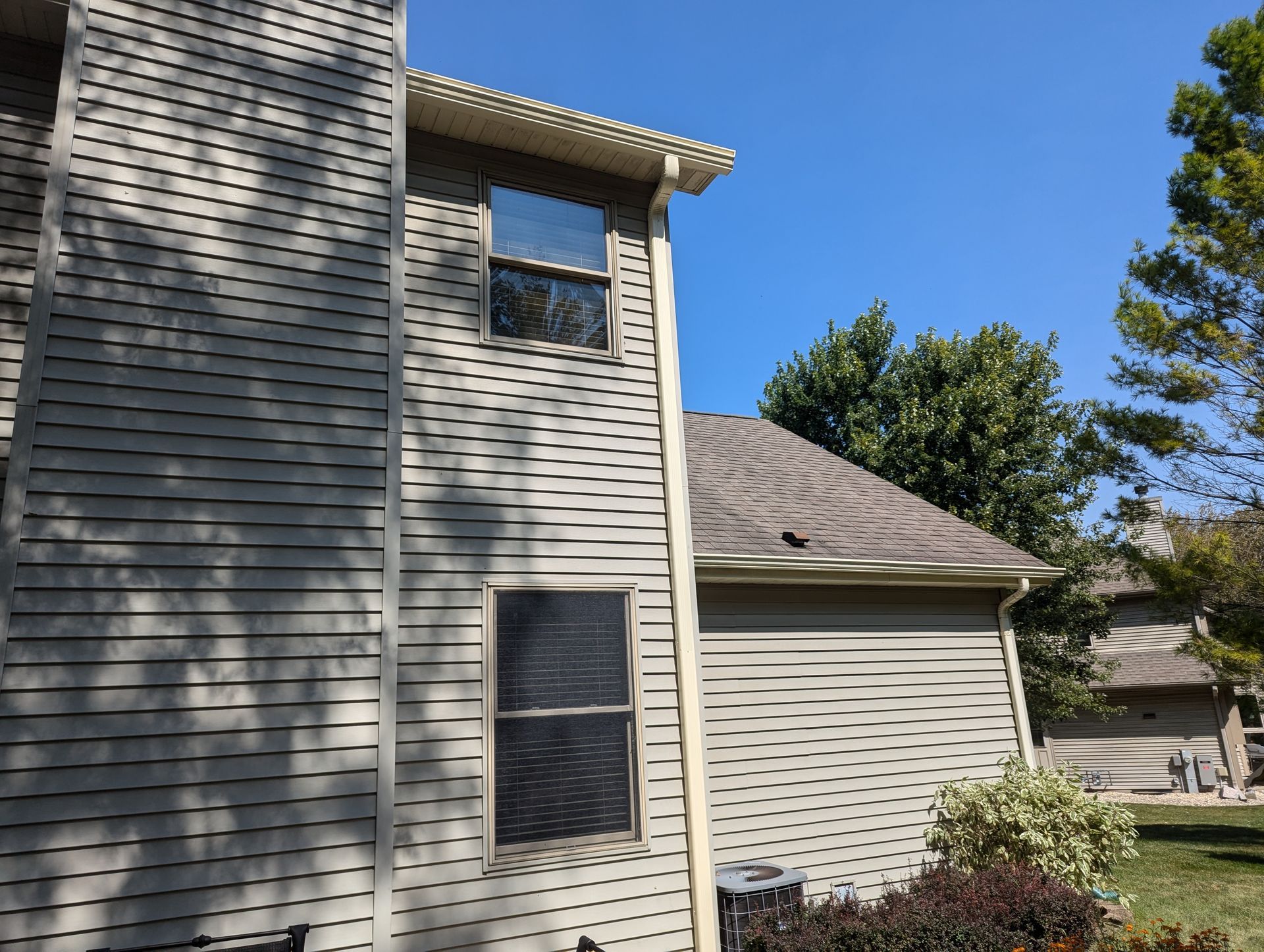 Exterior view of a two-story house with gray siding, two windows, and a roof, under a blue sky.