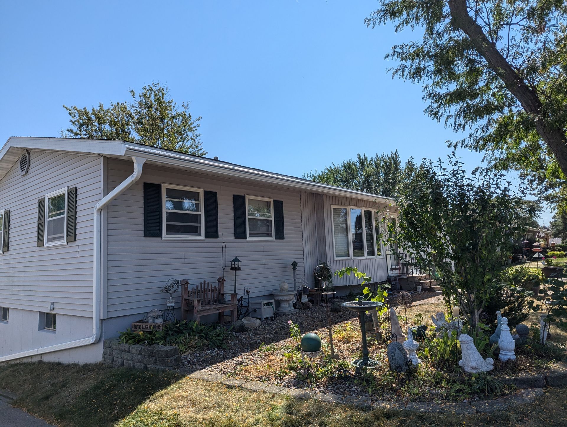 Tan house with black shutters, landscaping in front, under a clear blue sky.