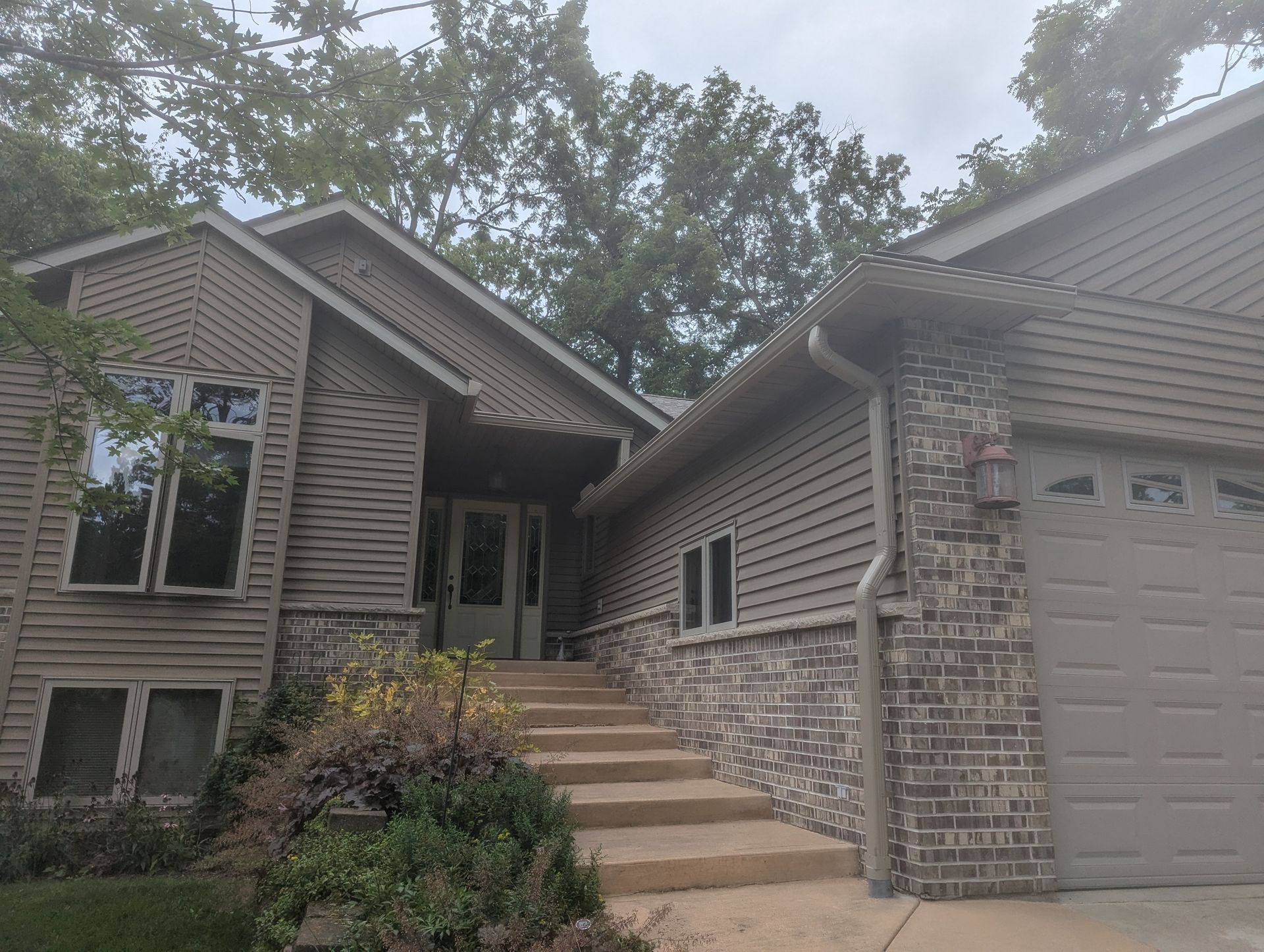 Brown house with stone accents, stairs leading to the front door, and a garage on the right side.