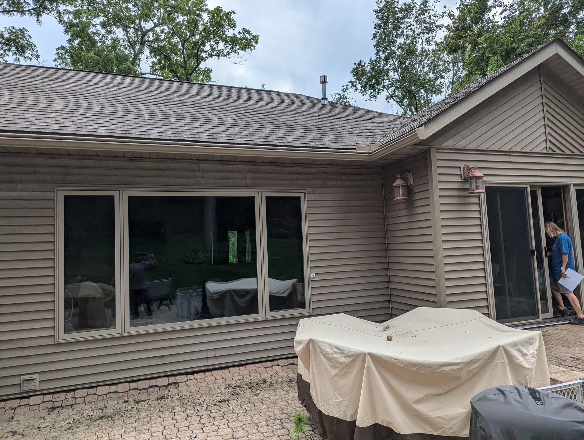 Exterior of a house with a large window and sliding door, beige siding, and a tan patio cover.