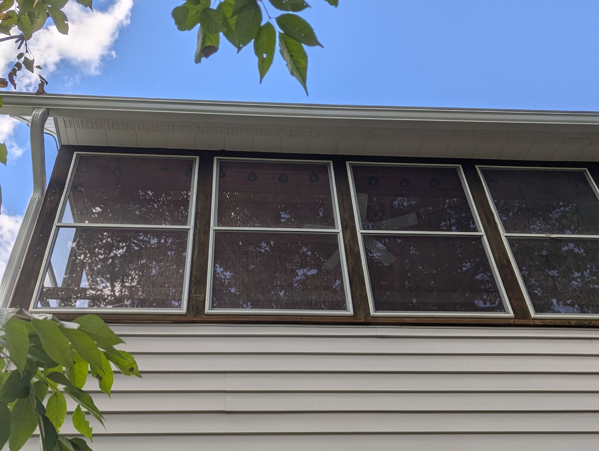Exterior view of a house with several rectangular screened windows under the roof's edge and white siding below.