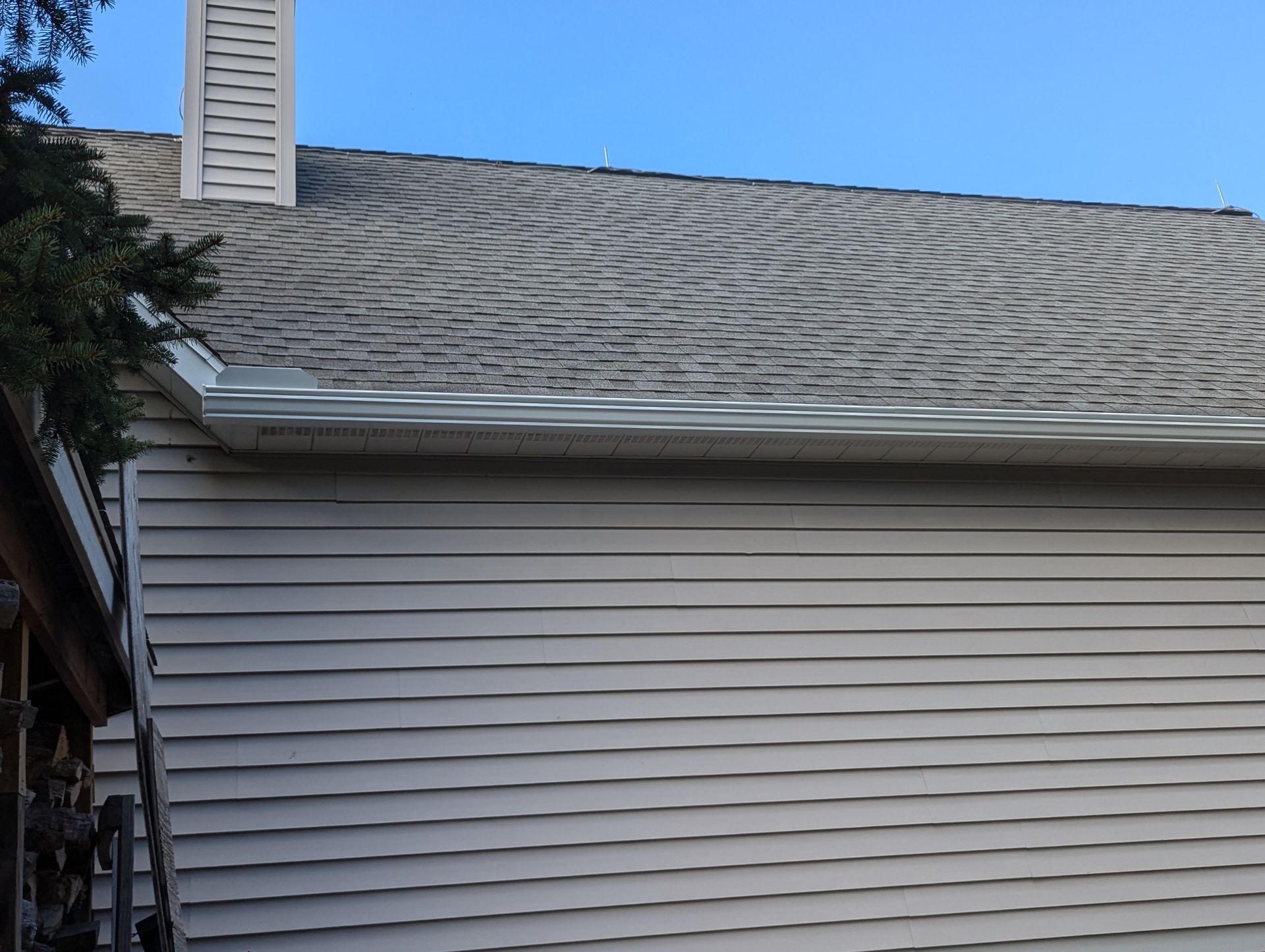 A house with a gray shingled roof and white siding under a clear blue sky.