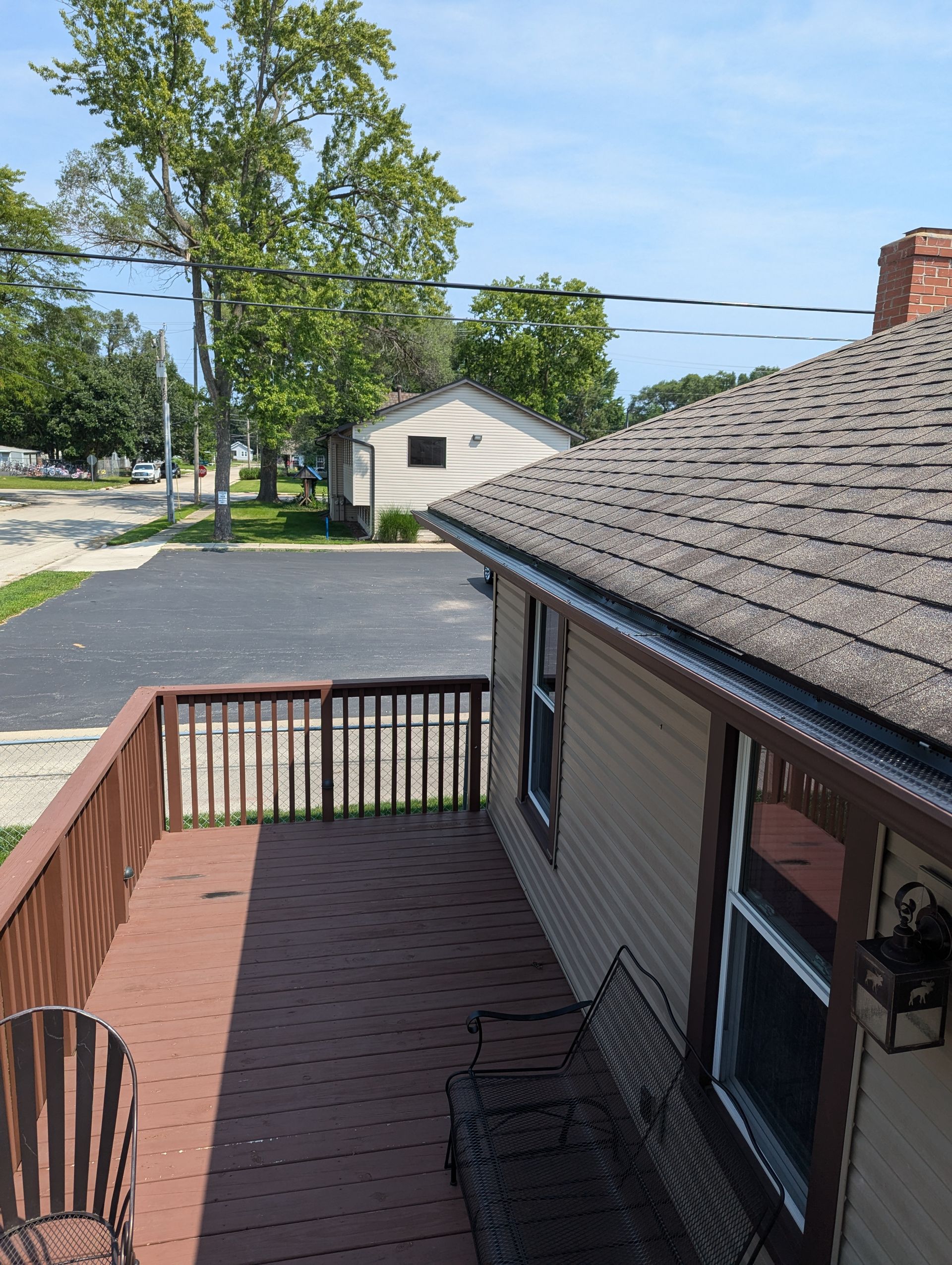 Wooden deck with brown railing, tan house, and street view.