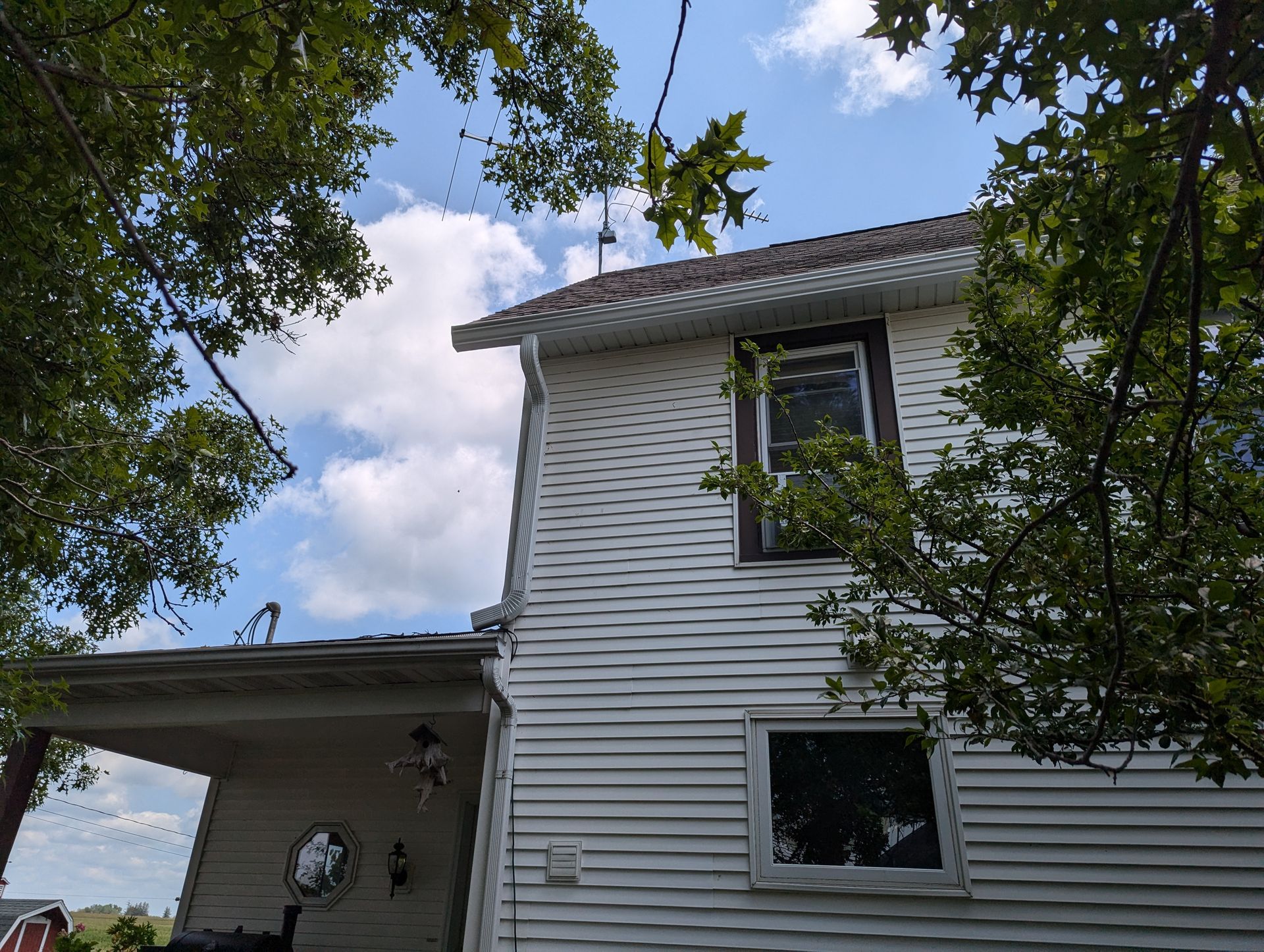 White house with porch and two windows against a partly cloudy blue sky.