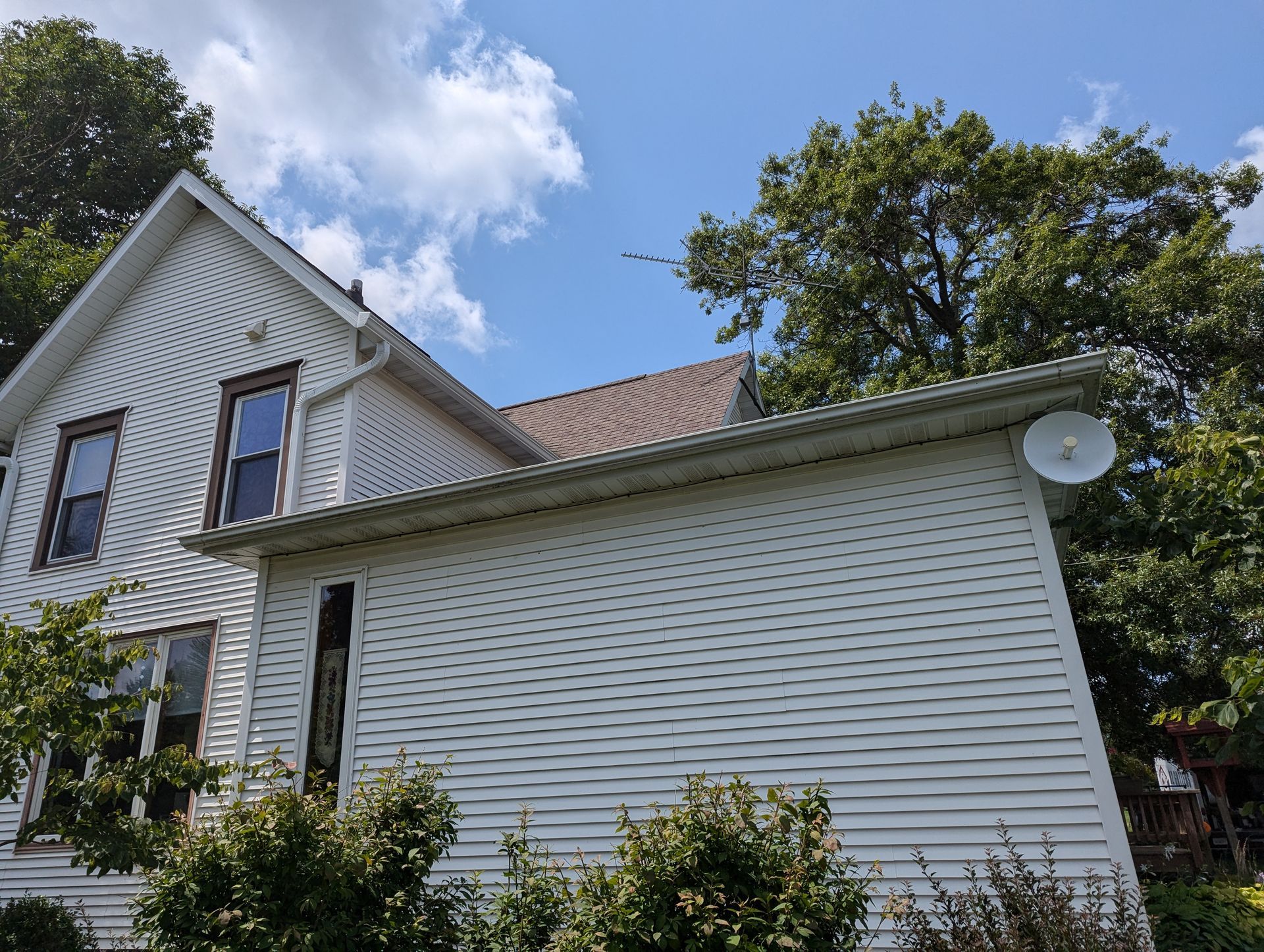 White house with white siding and brown roof under a blue sky. A satellite dish is mounted on the side.