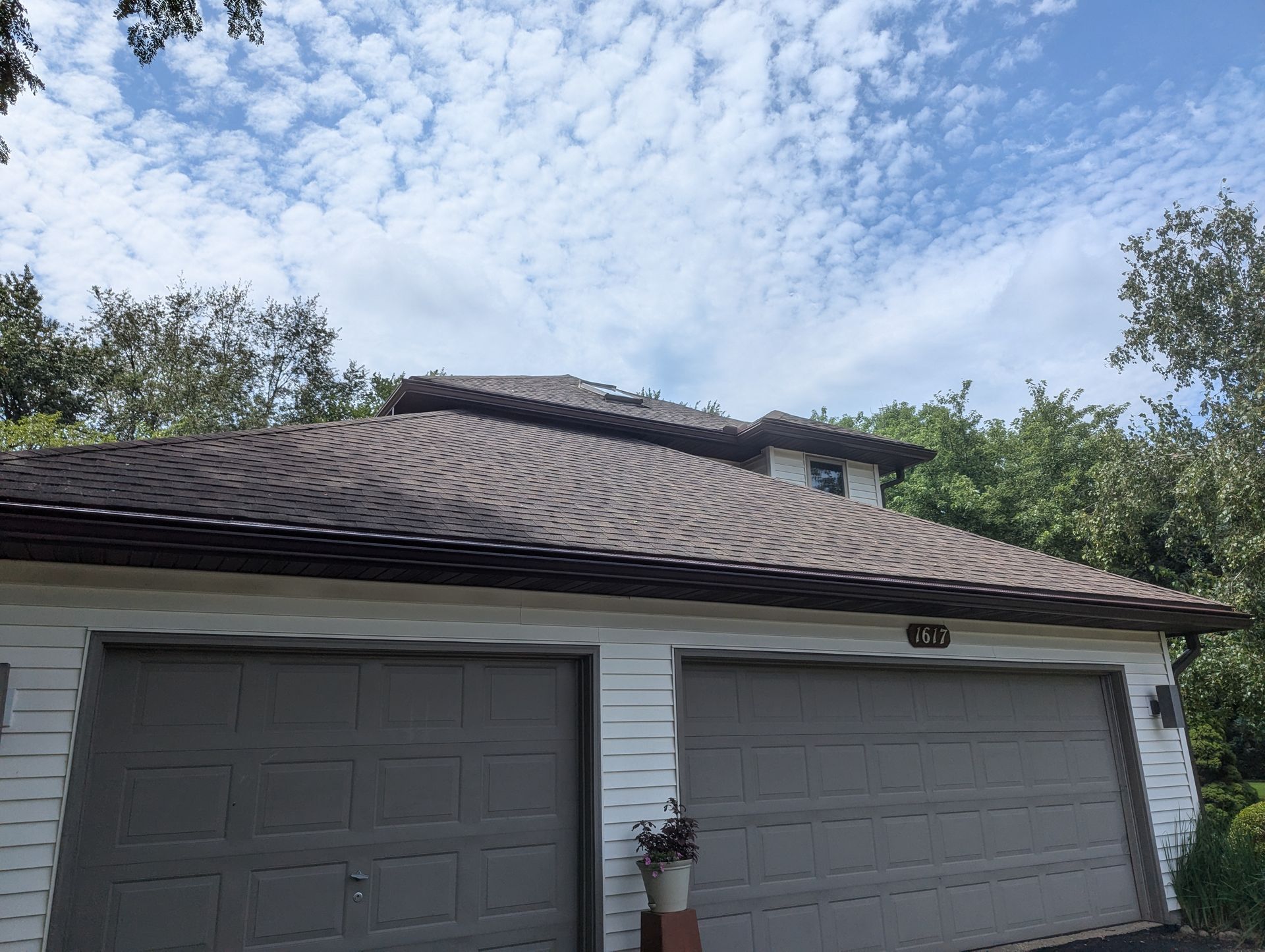 Garage with brown roof, two gray garage doors, and a blue cloudy sky.