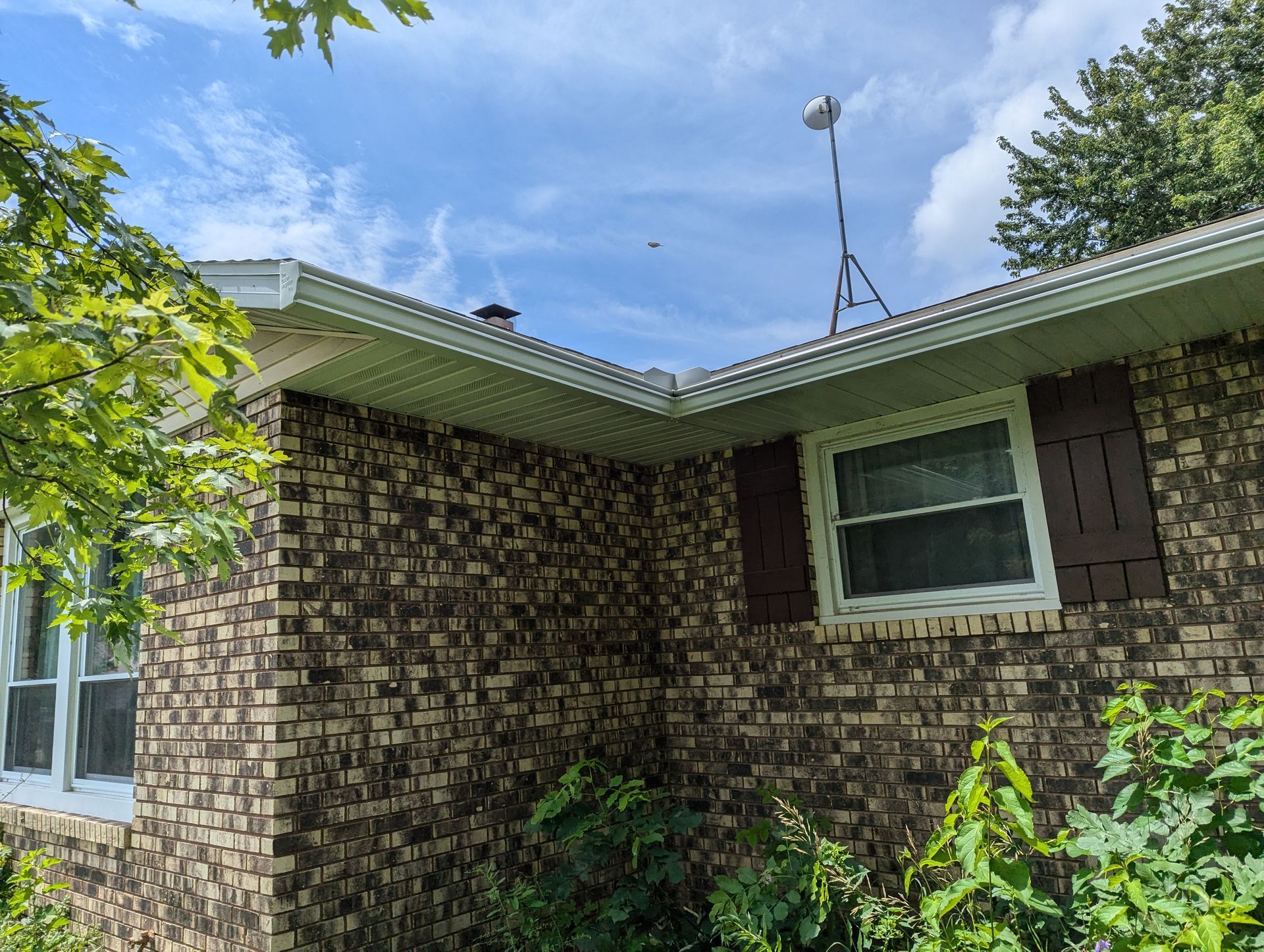 Brick house exterior with white gutters, brown shutters, and antenna. Overcast sky.