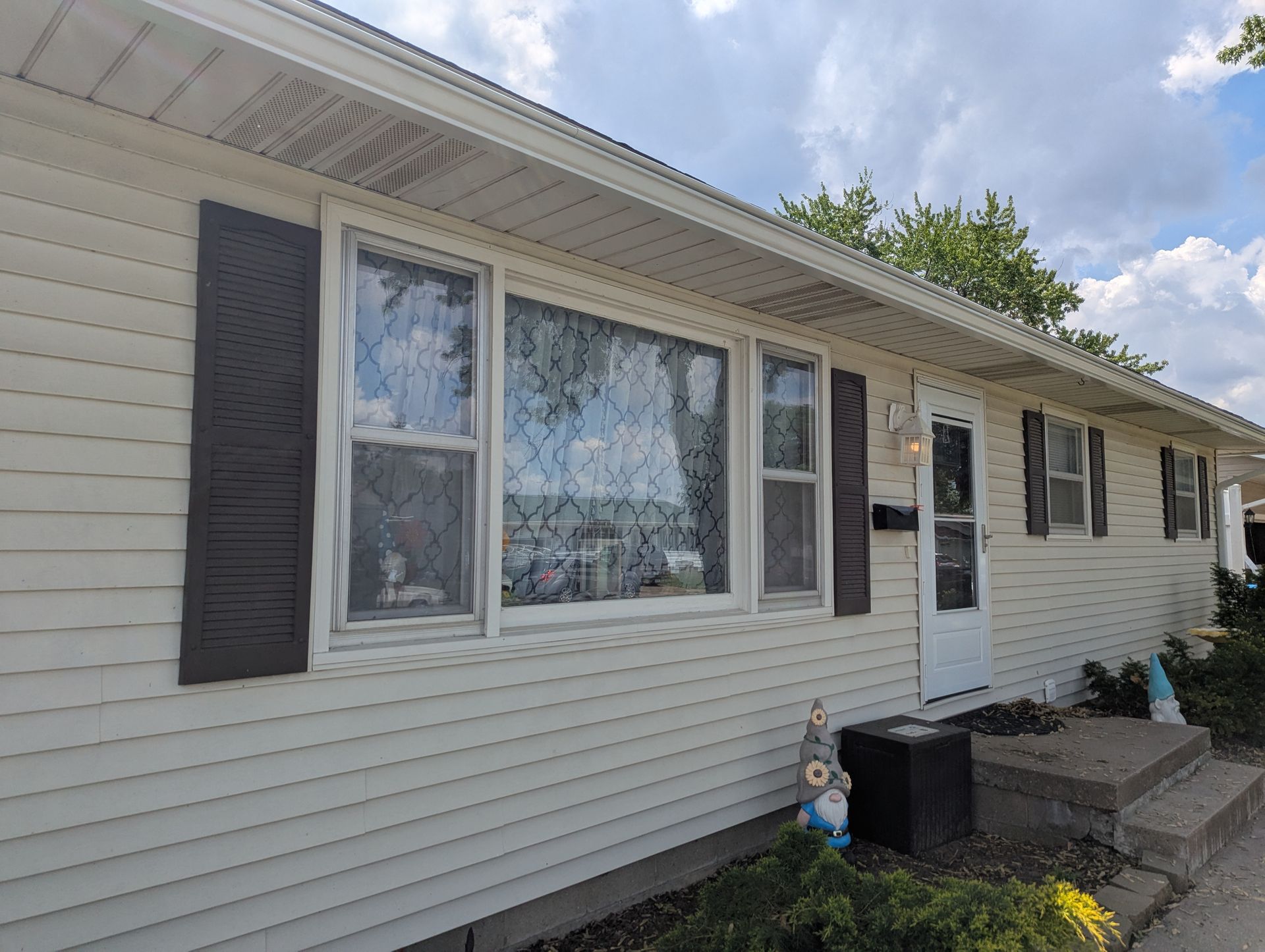 Beige house with brown shutters, front door, and steps under a cloudy sky.