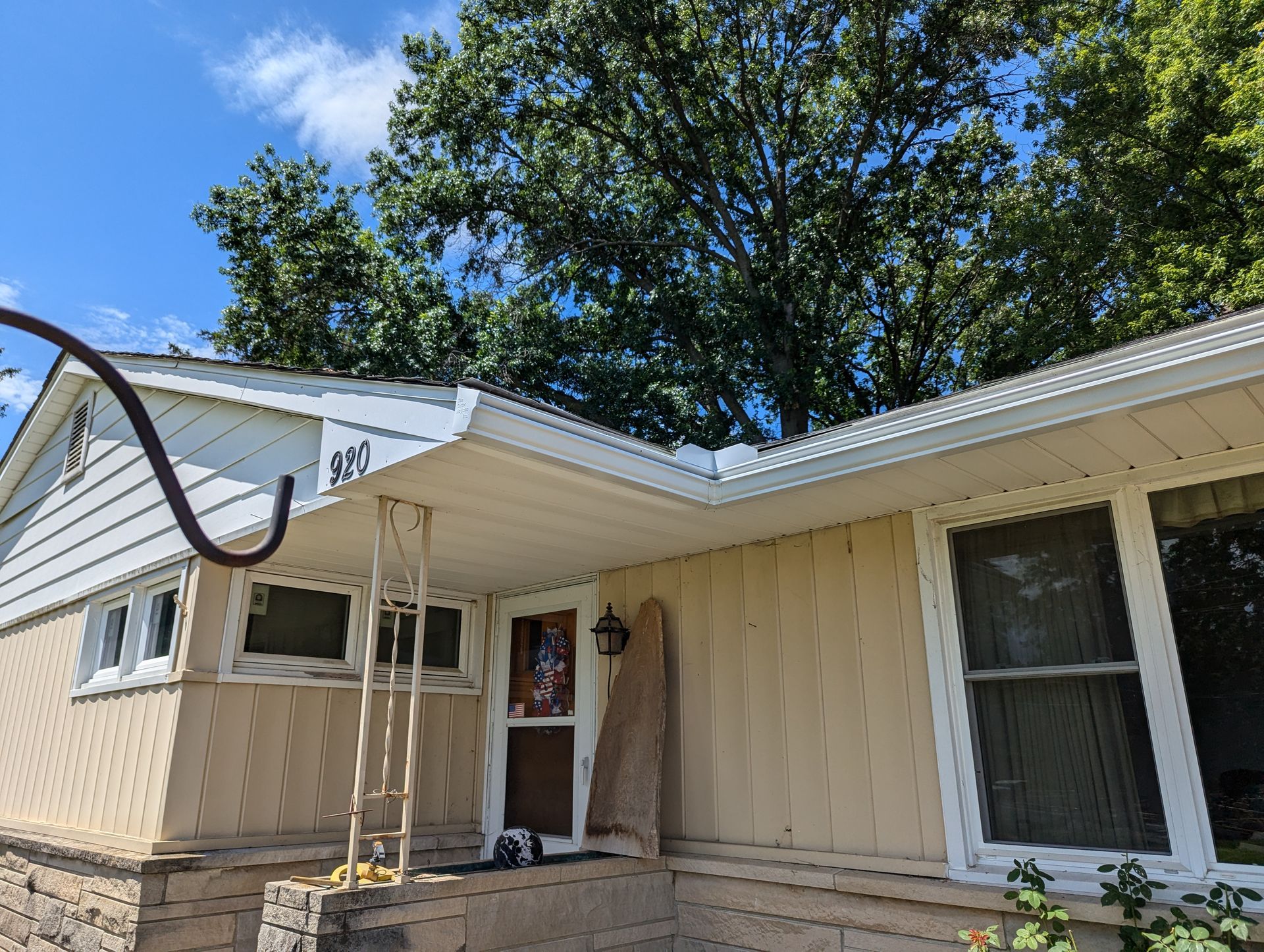 A house with tan siding, white trim, and a porch, with a blue sky and trees in the background.