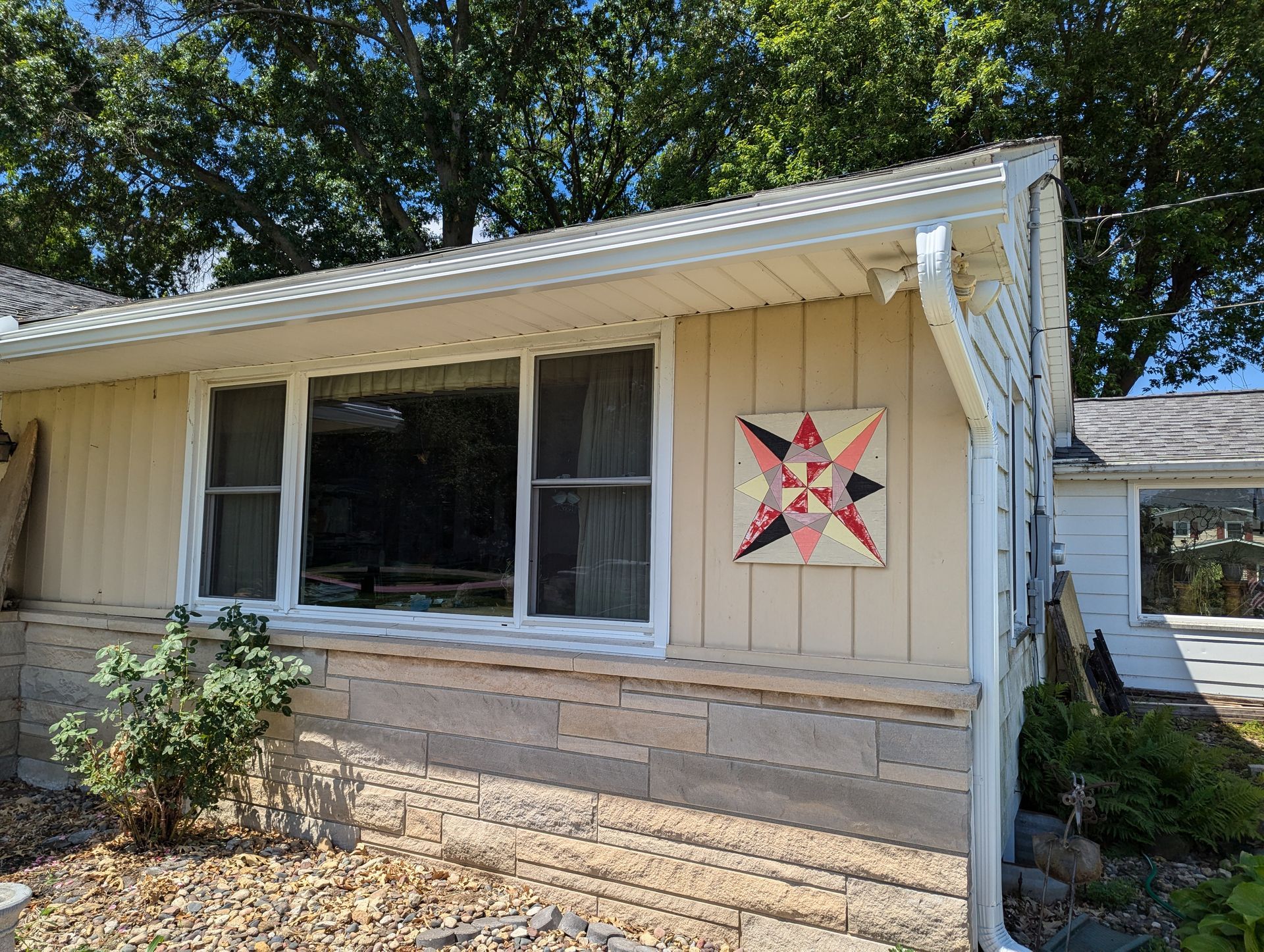 A tan house with a white-framed window and a quilt square decoration on the wall.