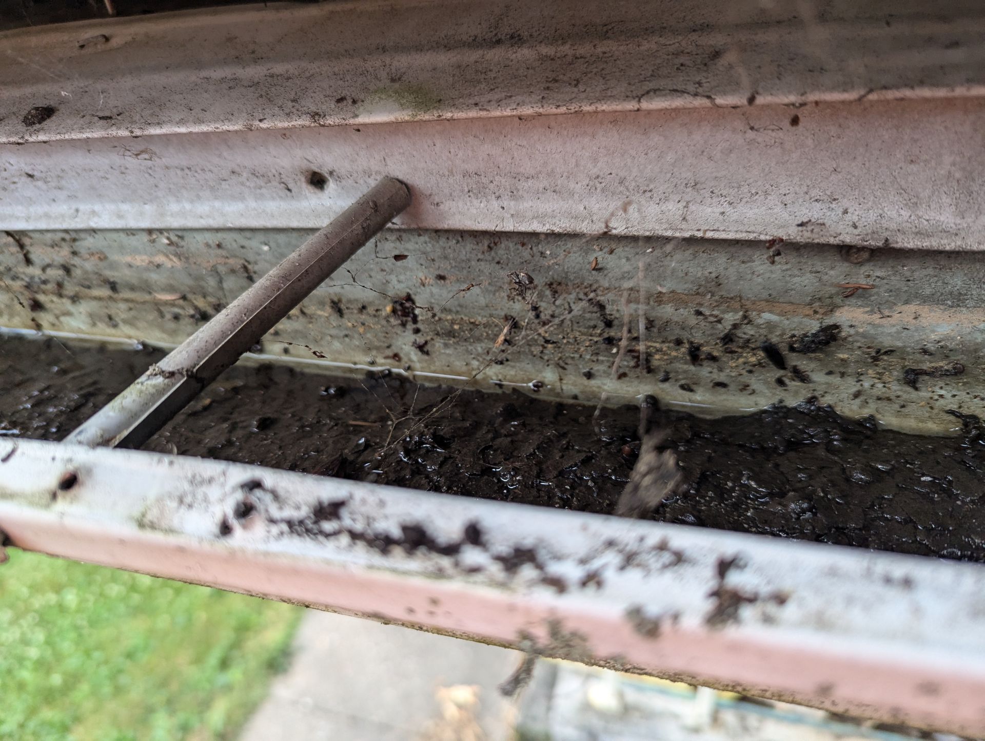 Dirty, clogged rain gutter with debris and a metal object.