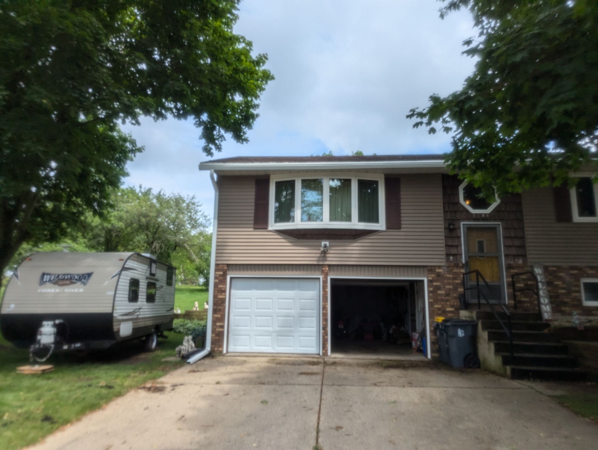 Two-story house with a white garage door, brown siding, and an RV parked on the lawn.