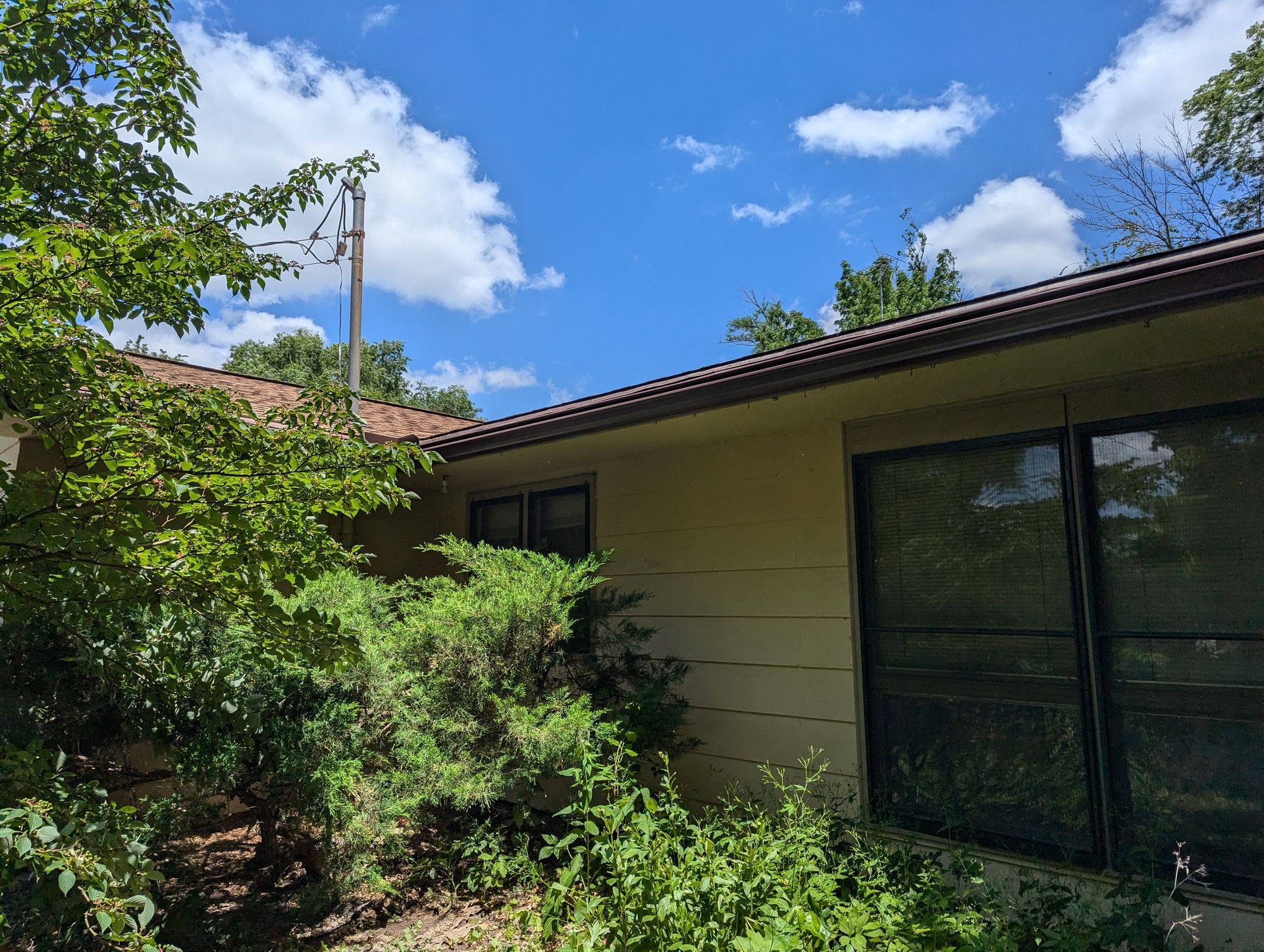 House exterior with trees and a blue sky with clouds.