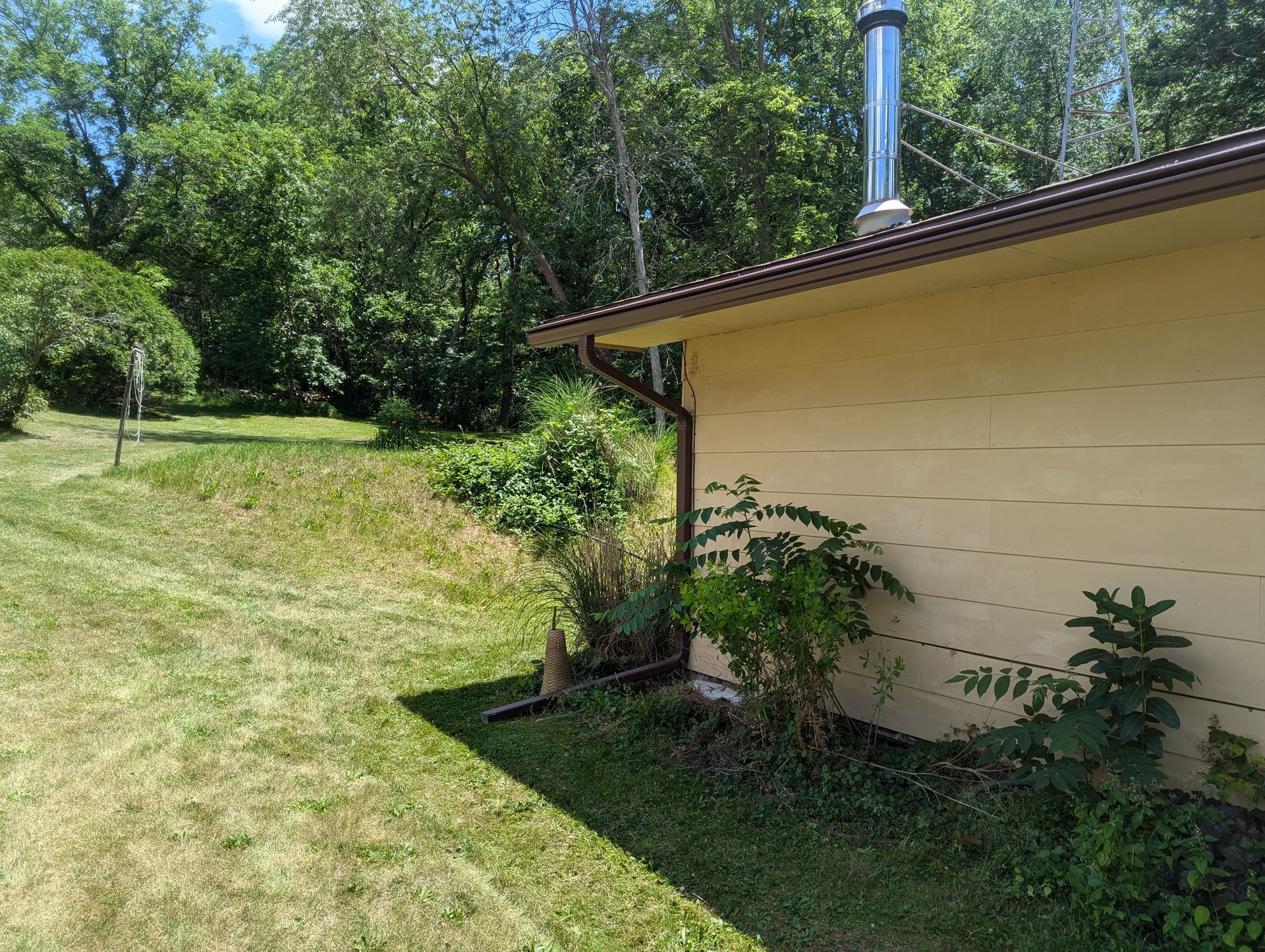 A tan building with a brown roof and a green grassy yard in a wooded area.