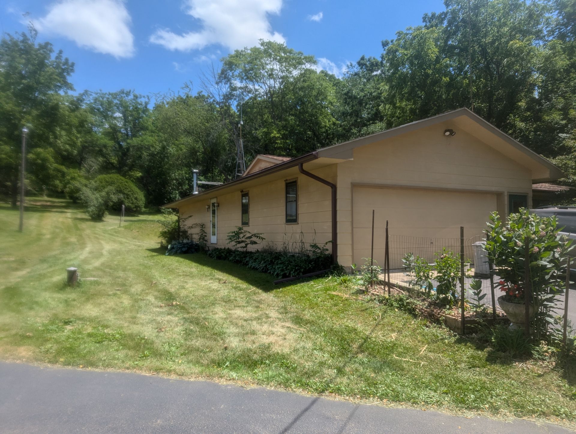 Tan house with attached garage, surrounded by green grass and trees, under a blue sky.