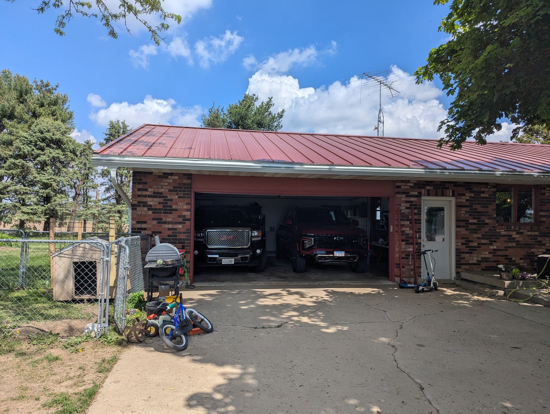 Two-car garage with red roof, two trucks parked inside, and various objects in front.