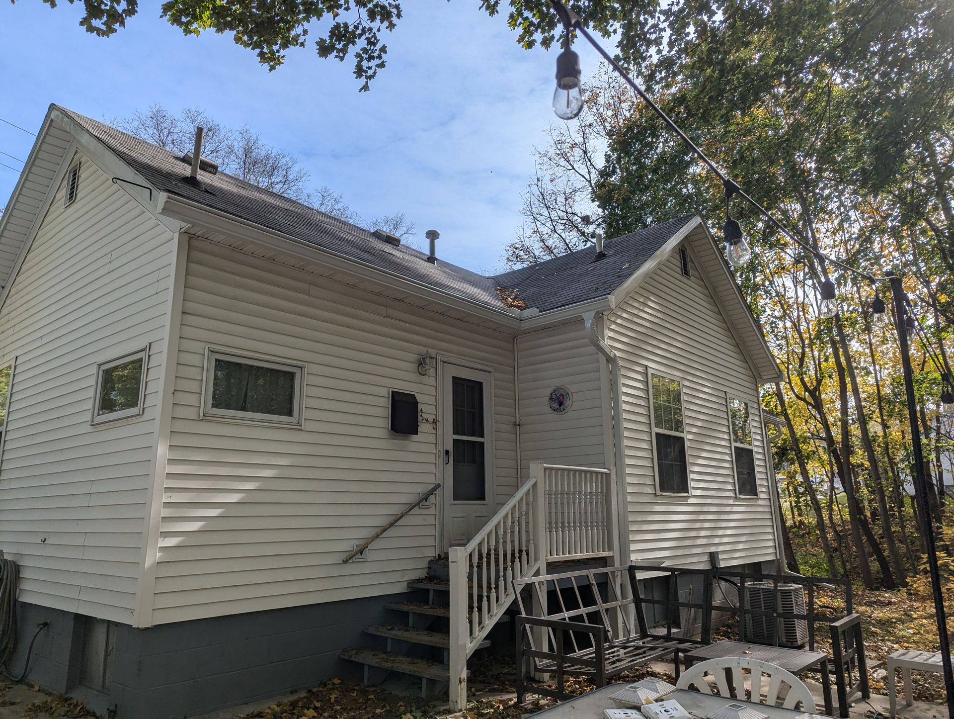 White house with front steps, side porch, and surrounding trees.