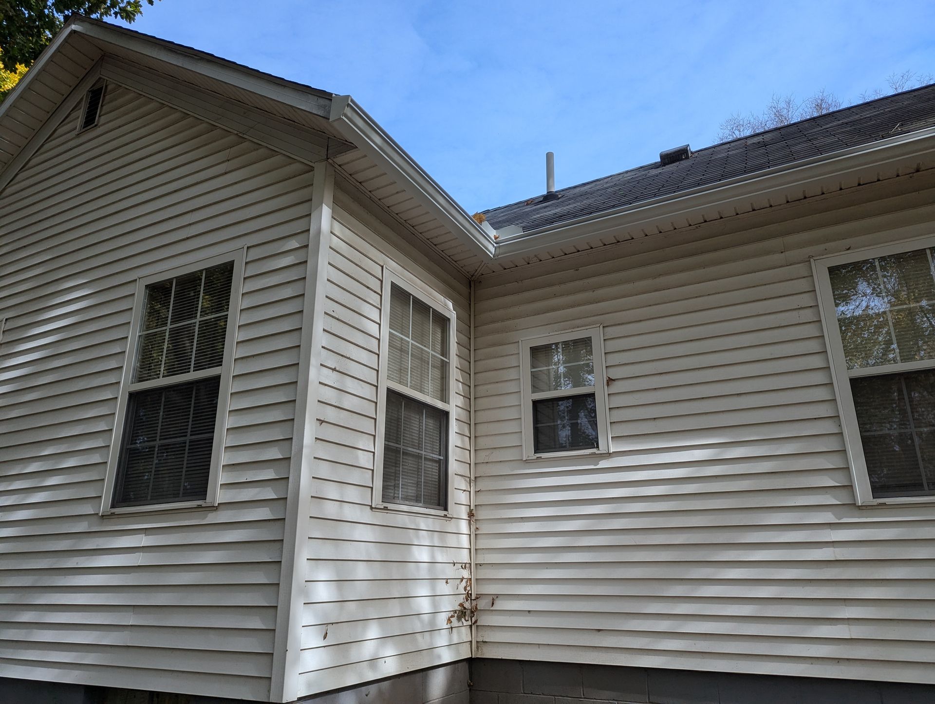Off-white siding of a house with multiple windows and dark roof, under a blue sky.