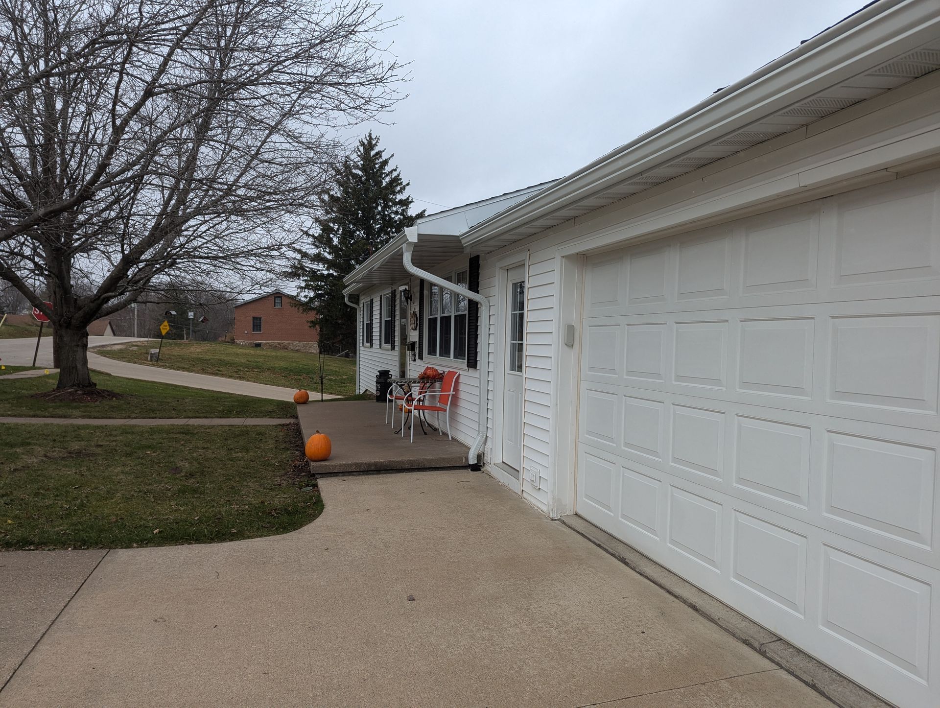 White house with attached garage; concrete driveway and walkway. Pumpkins on porch. Overcast day.