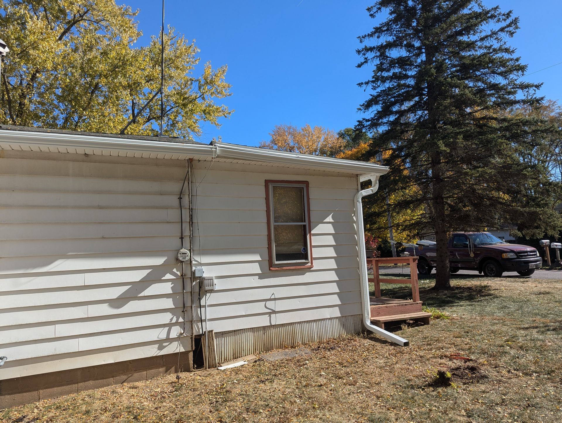 White-sided building with a window and a red truck parked outside on a sunny day.