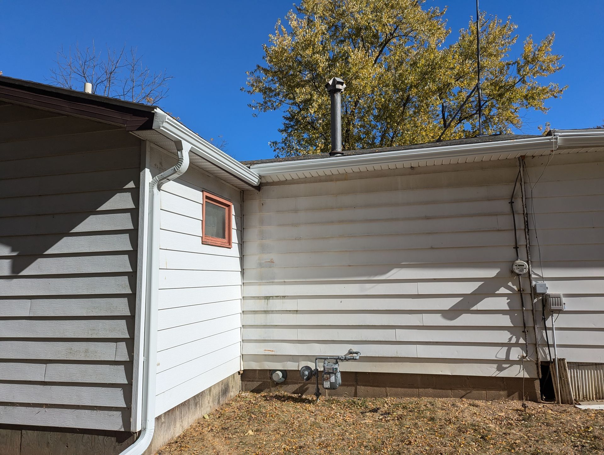 White-sided house exterior with a small window, gutter, and a chimney against a blue sky.