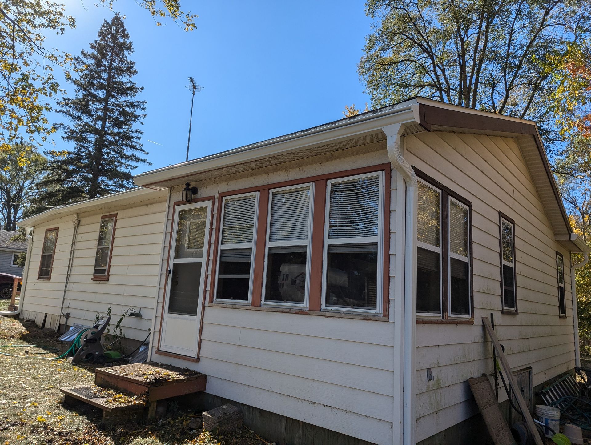 Beige house with a white roof, several windows, and an antenna on a bright sunny day.