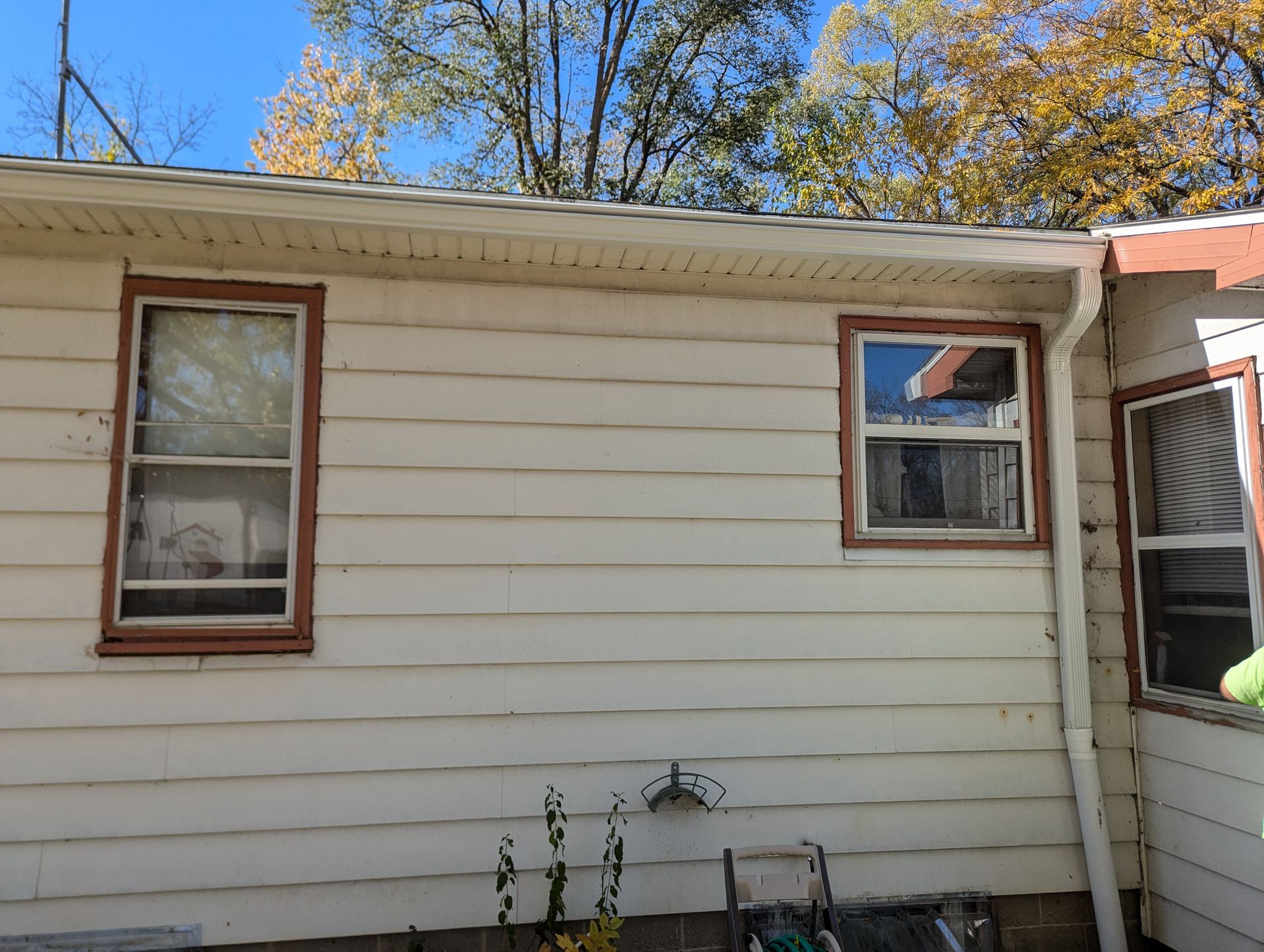 Exterior wall with three windows, white siding, brown trim, and trees in background.