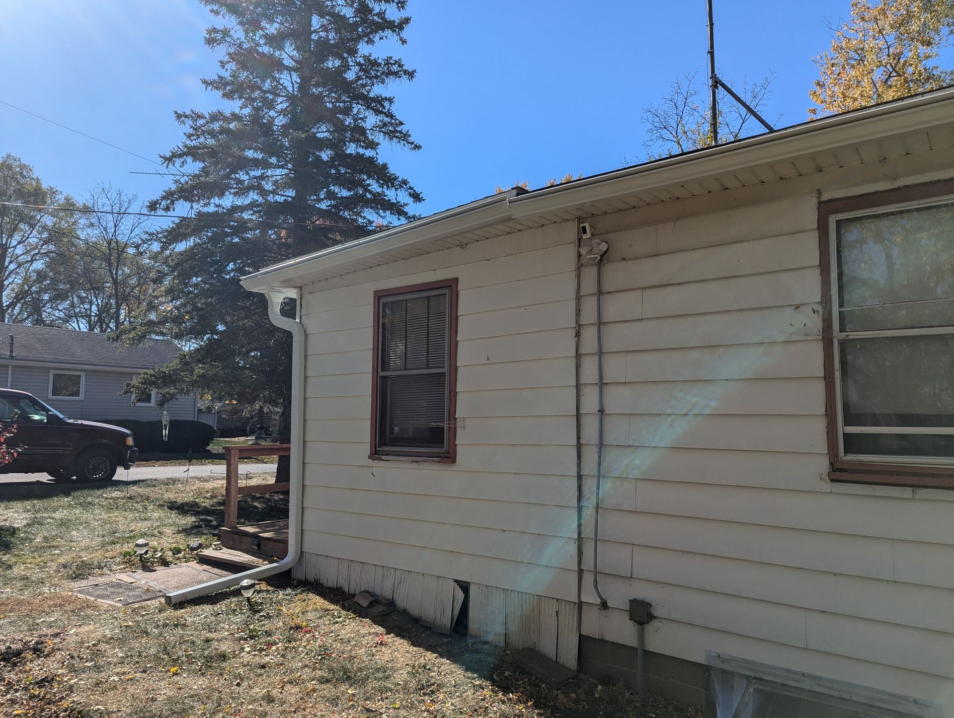 Side view of a house with white siding, two windows, and a gutter, on a sunny day.