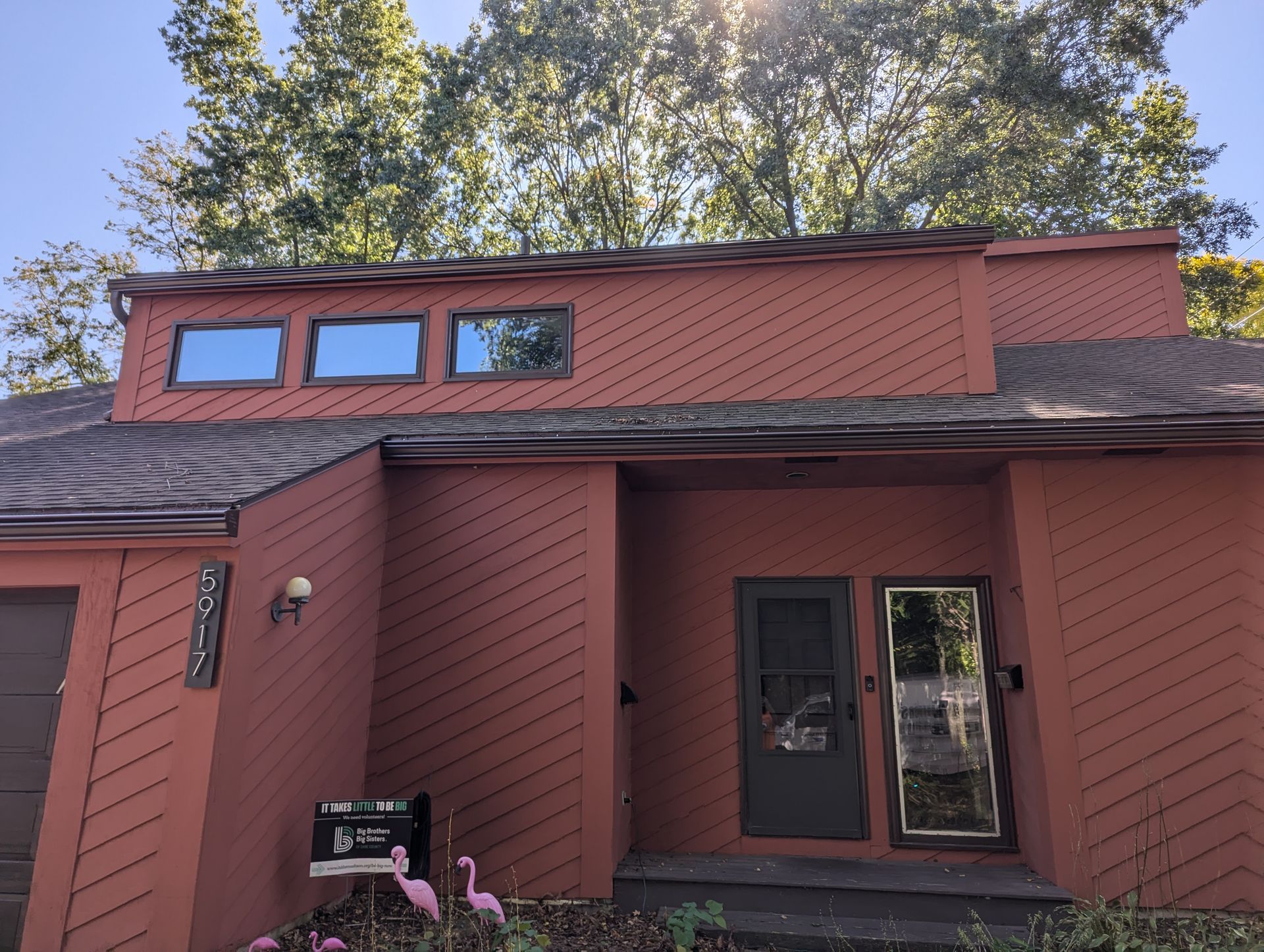 Red house with small windows, dark door, and trees in the background under a blue sky.