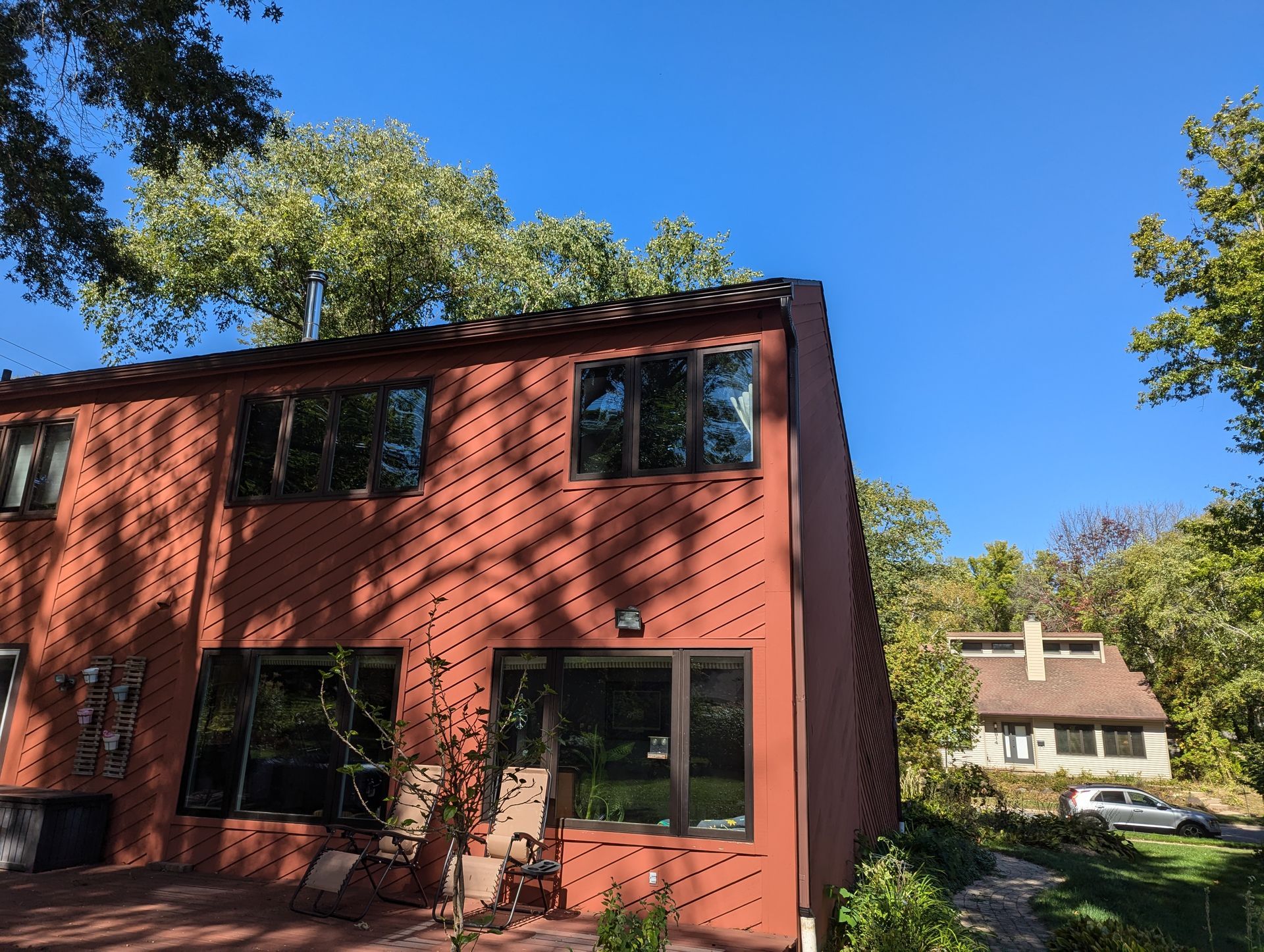 Red townhome exterior with dark windows, terracotta roof, and trees under a clear blue sky.