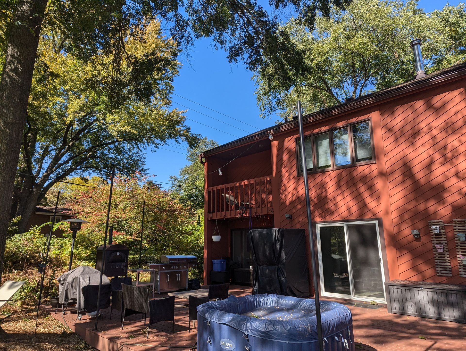Red brick house with a deck, hot tub, and fall foliage against a blue sky.