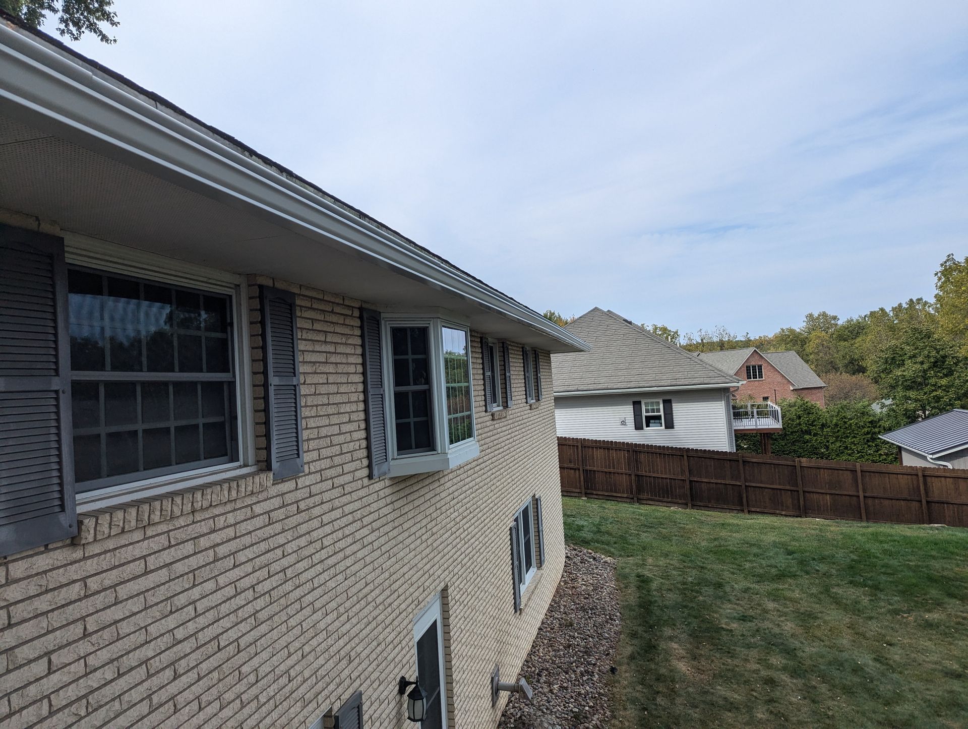 Brick house exterior with gray shutters, gutters, and a grassy yard.