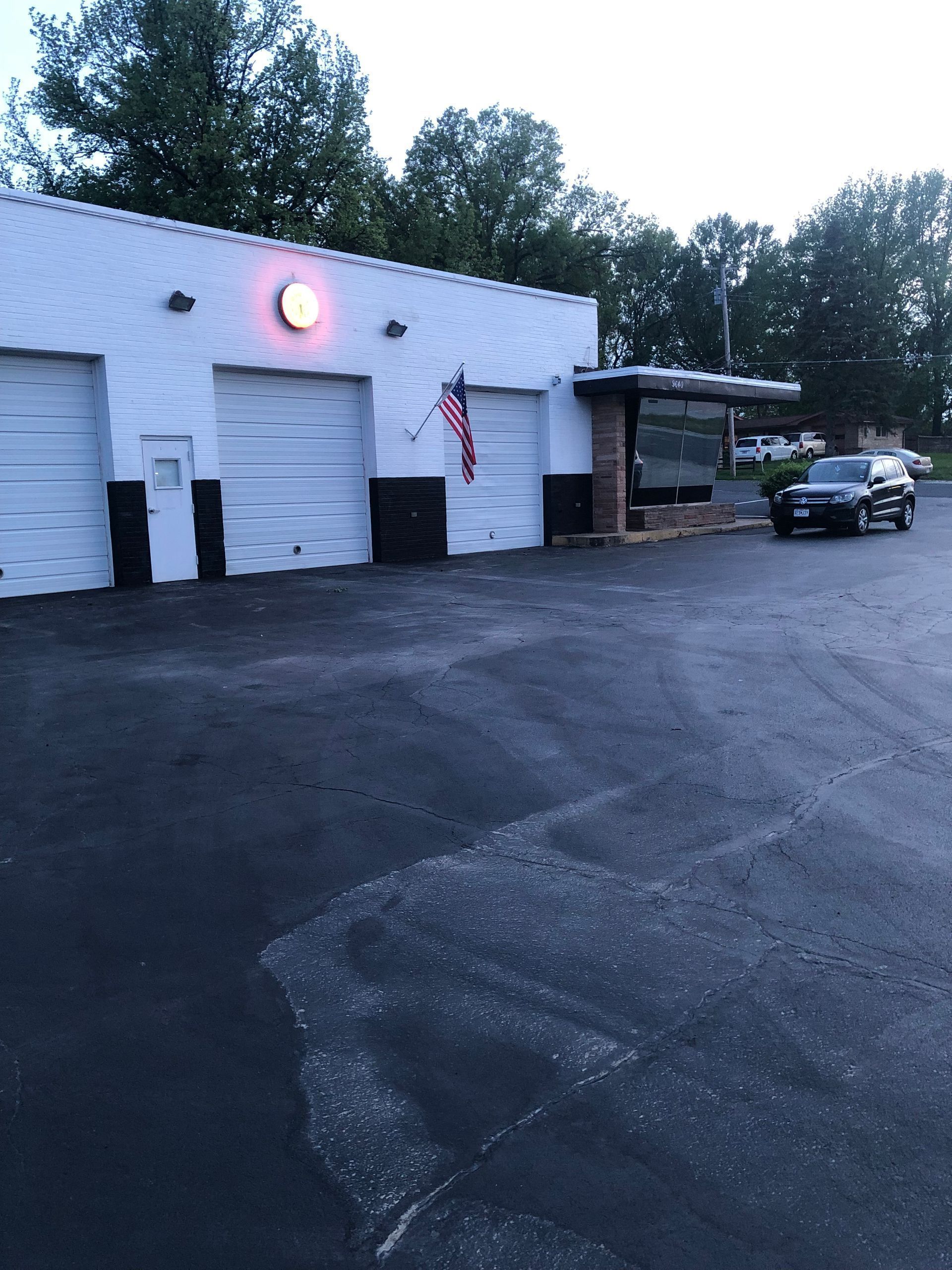 A car repair shop with closed garage doors and a black SUV parked outside.