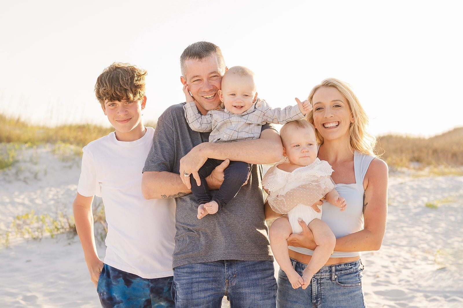 Family of five smiling on a beach, two babies being held.