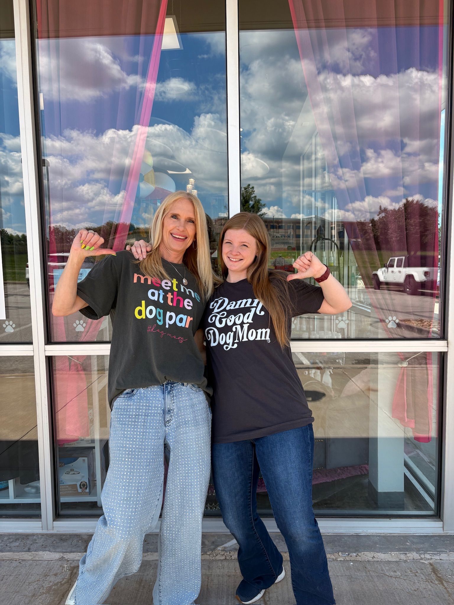 Two people posing and smiling outside a storefront, wearing dark T-shirts and raising their fists.
