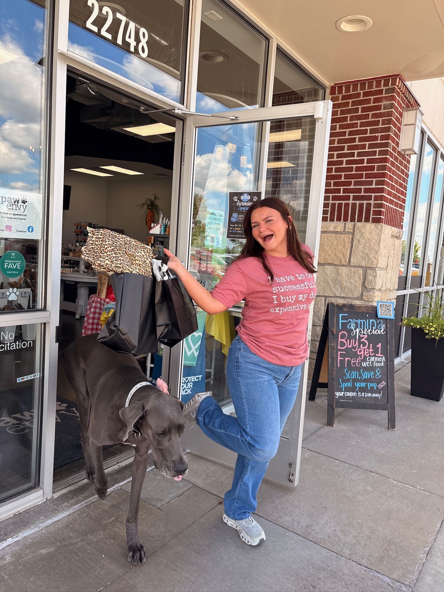 Woman and dog at storefront entrance, woman smiling and holding a bouquet while a large gray dog steps outside.