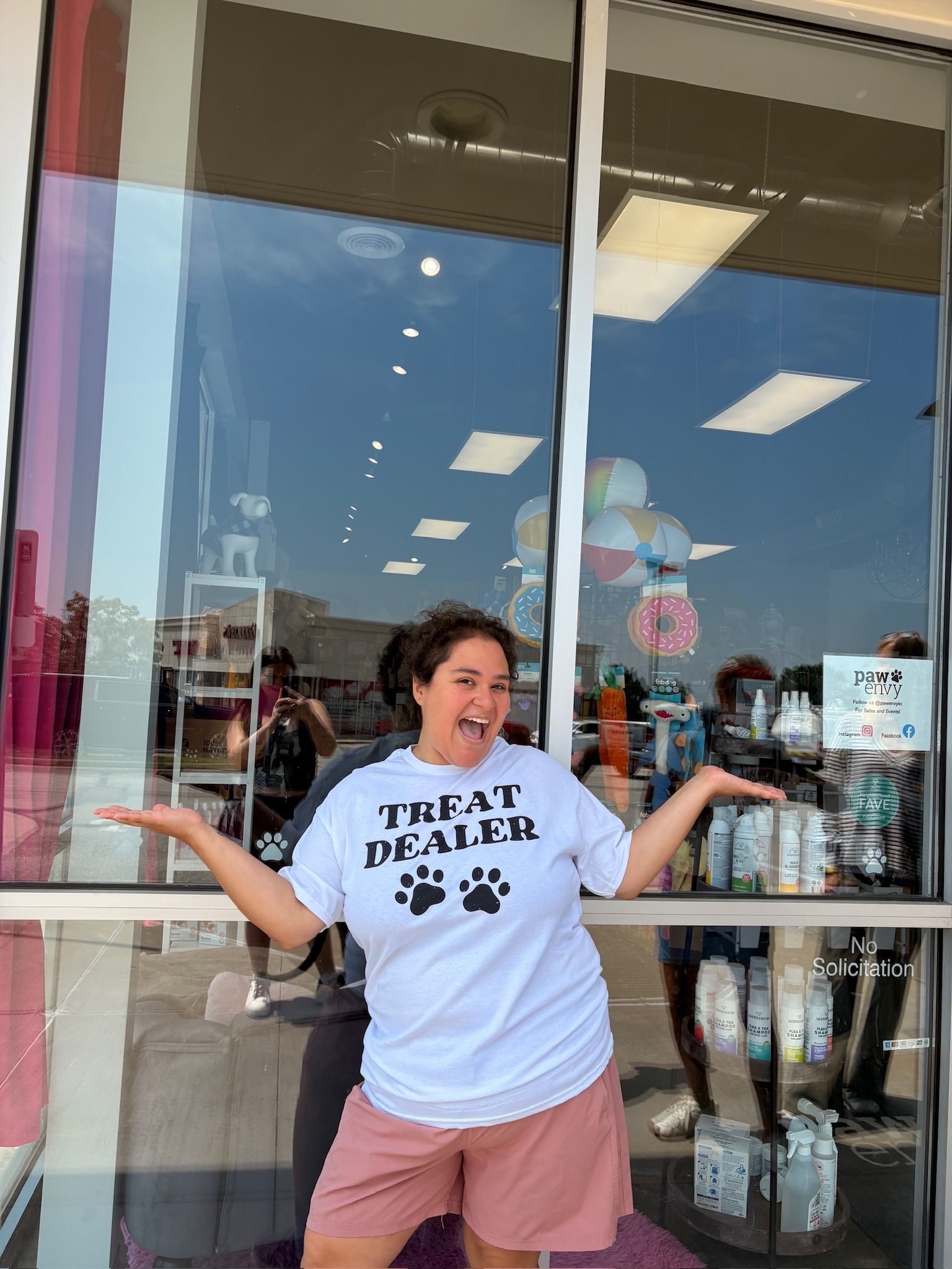 Woman posing outside a store with arms out, wearing a white graphic T-shirt and pink shorts.