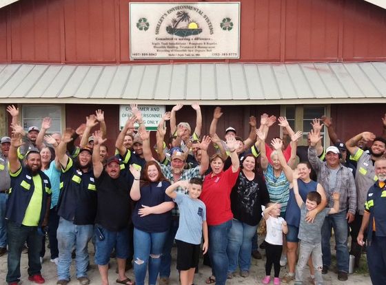 A large group of people are standing in front of a building with their hands in the air.