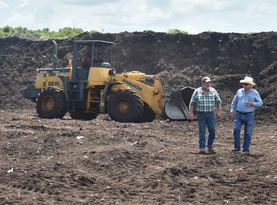 Two men are standing in front of a bulldozer in a dirt field.