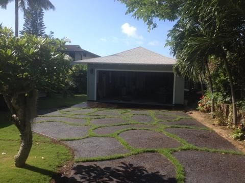 Driveway with patterned paving leading to a modern house and garage, framed by trees and greenery