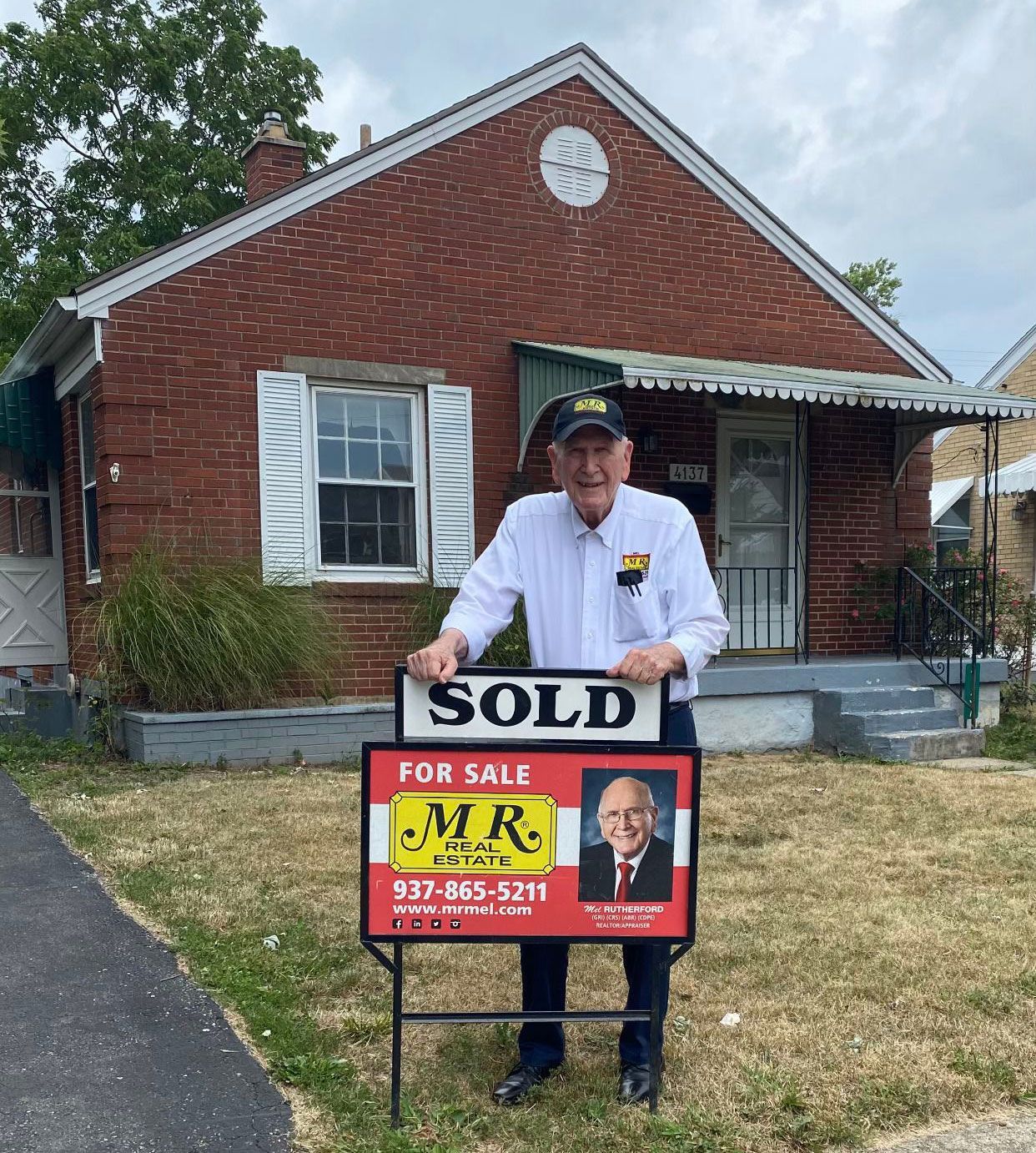 A man holding a sold sign in front of a brick house