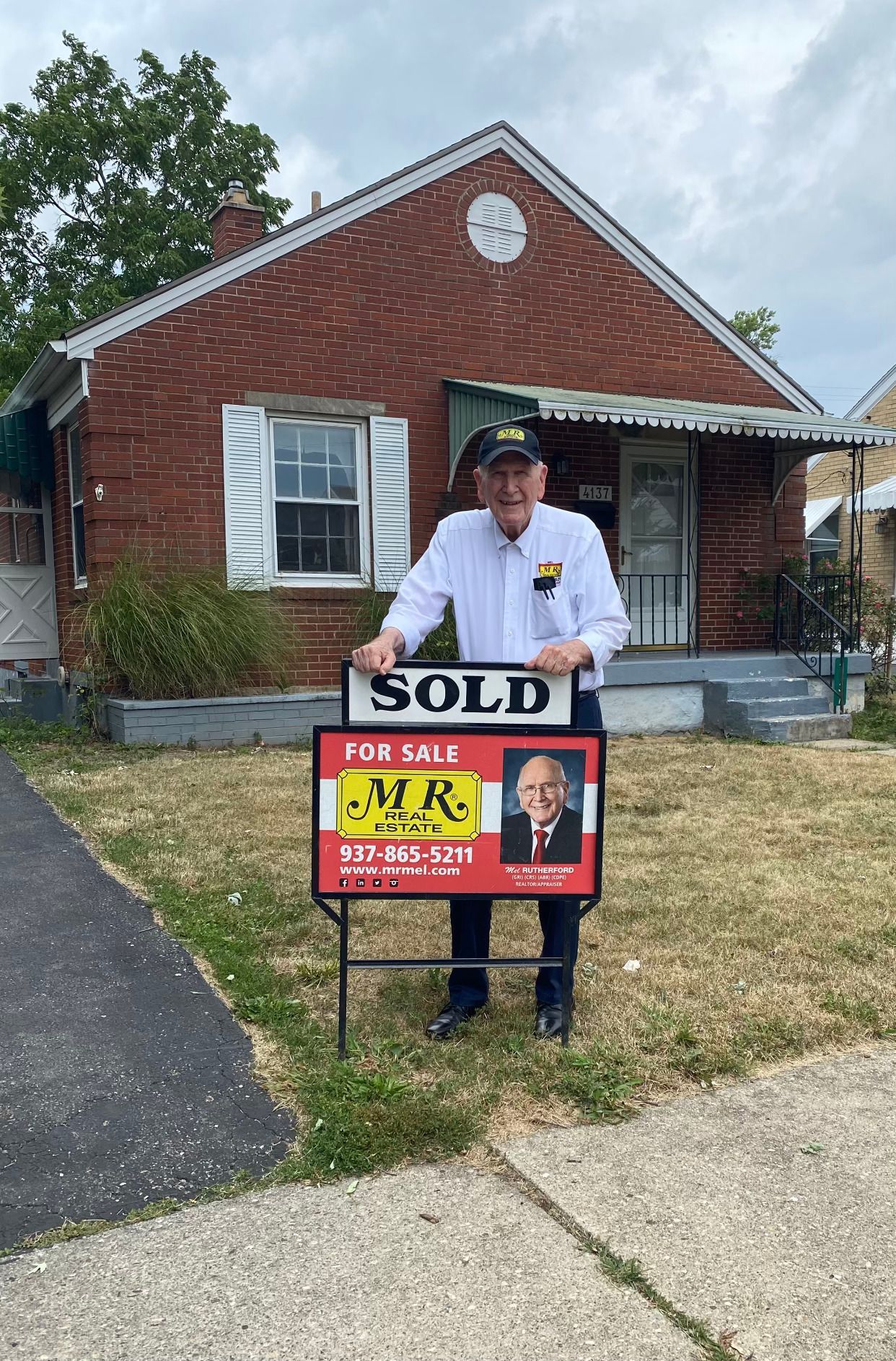 A man is holding a sold sign in front of a brick house.