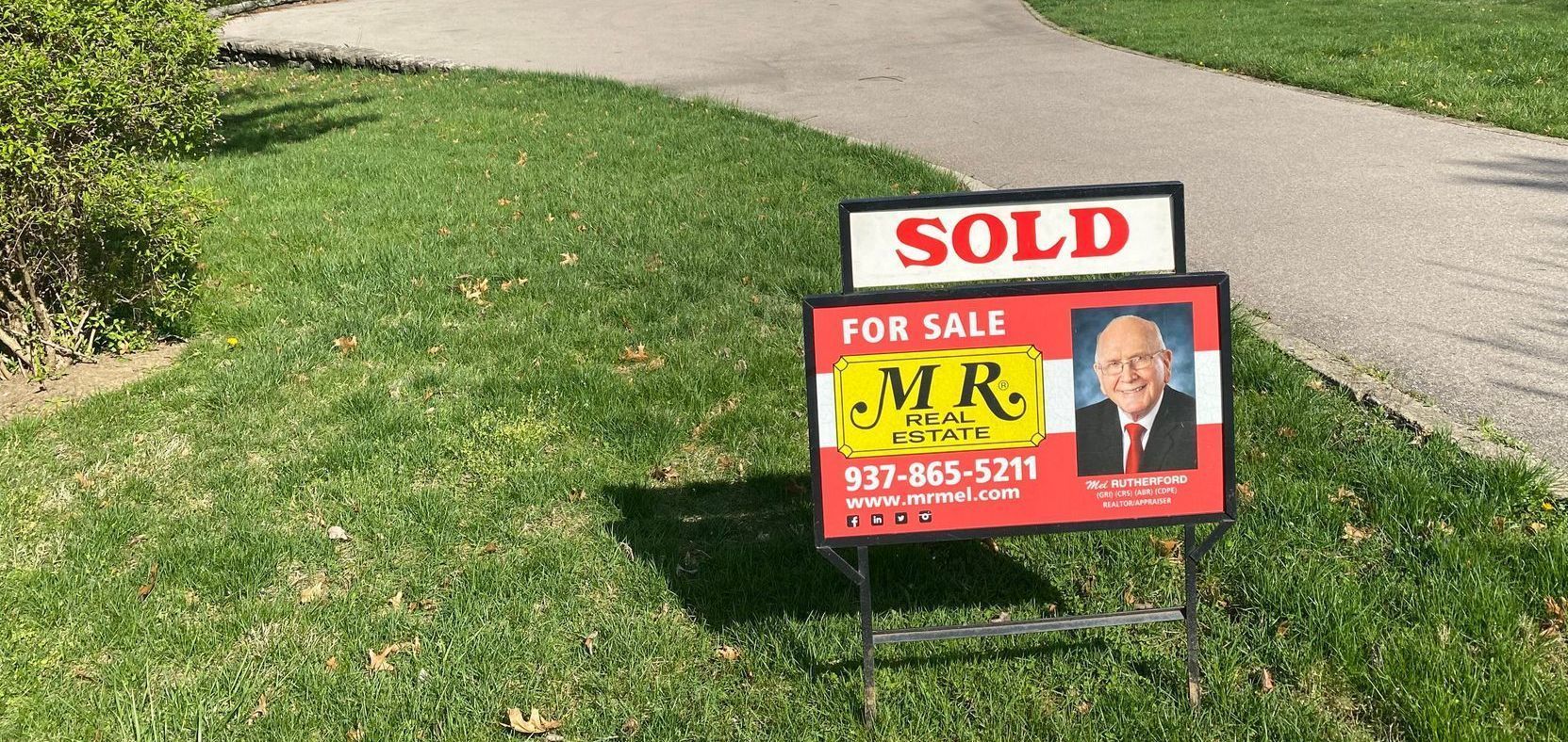 A sold sign is sitting in the grass next to a sidewalk