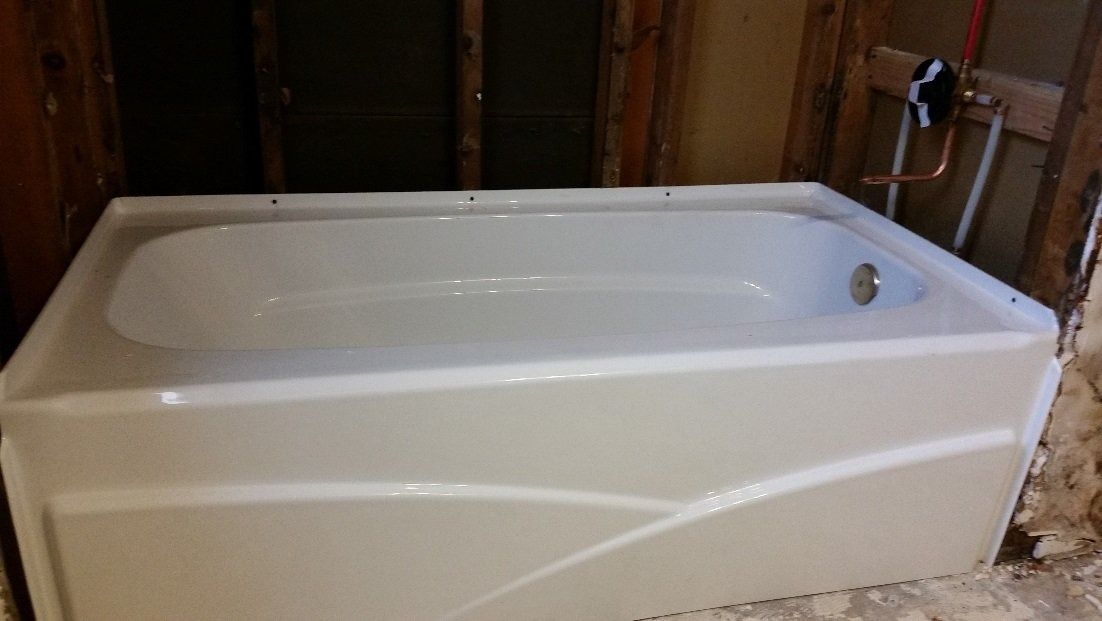 White bathtub in a bathroom under construction, with exposed walls and unfinished flooring.