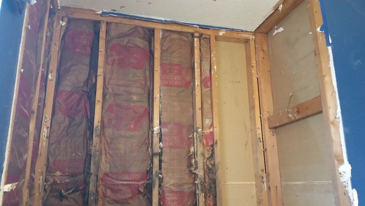 Partially opened wall revealing exposed insulation, studs, and yellow drywall in a home interior