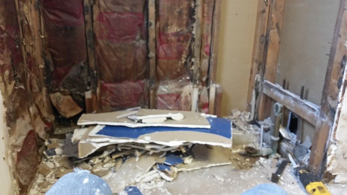Damaged room with exposed insulation, broken drywall, and debris scattered on the floor.