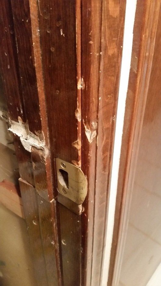 Close-up of a damaged wooden door frame with chipped paint and a metal latch.