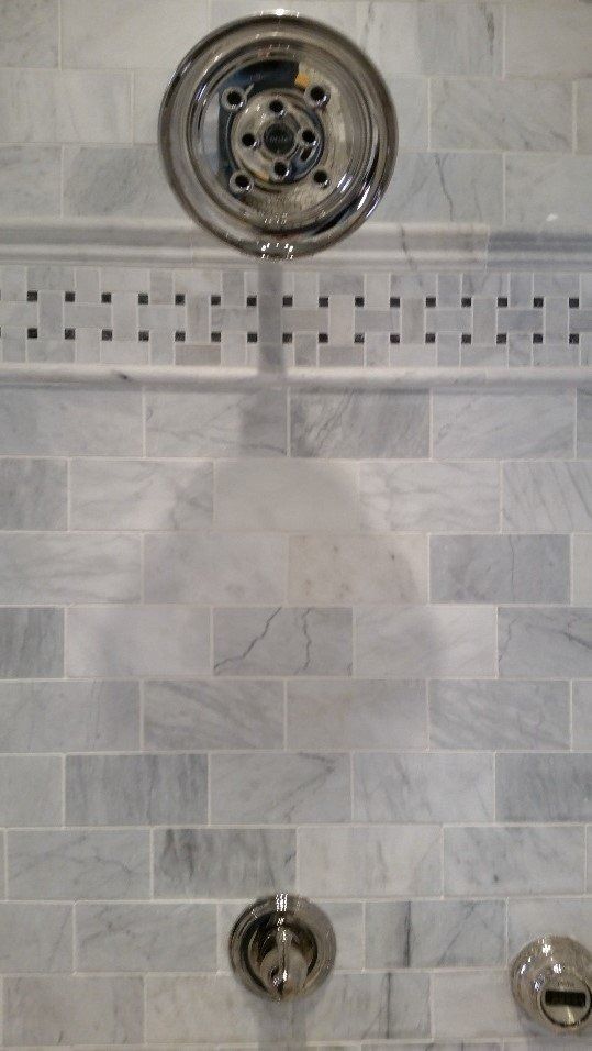 Shower wall with gray tile and visible plumbing fixtures, including showerhead and control handles.