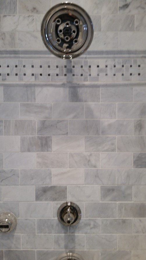 Gray tiled shower wall with chrome shower valve, round shower head connection, and lower control handle