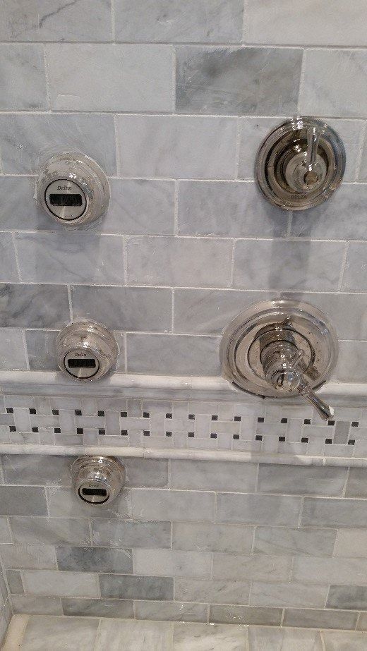 Shower wall with chrome control knobs and a small built-in shelf on light gray tile.